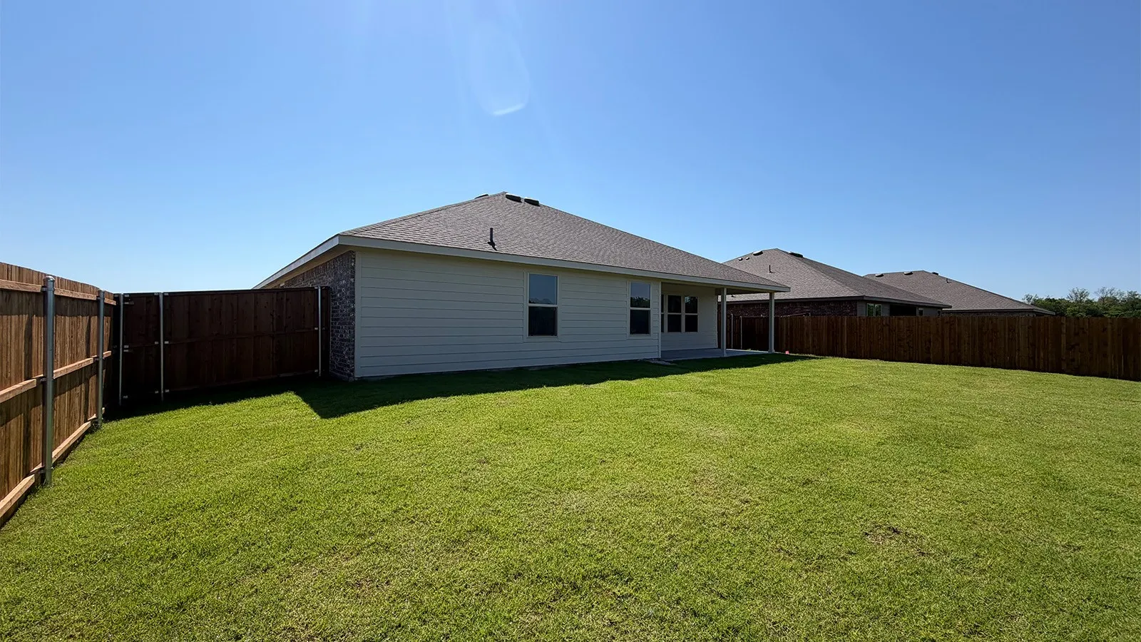 Spacious backyard featuring a manicured lawn, full perimeter wood fencing, and a covered patio area