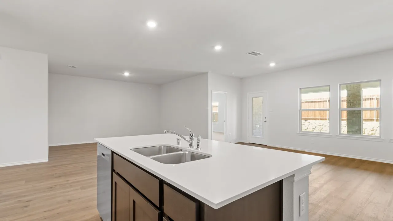Kitchen island featuring a double-basin stainless steel sink, a chrome faucet, and integrated dishwasher, all topped with a white countertop