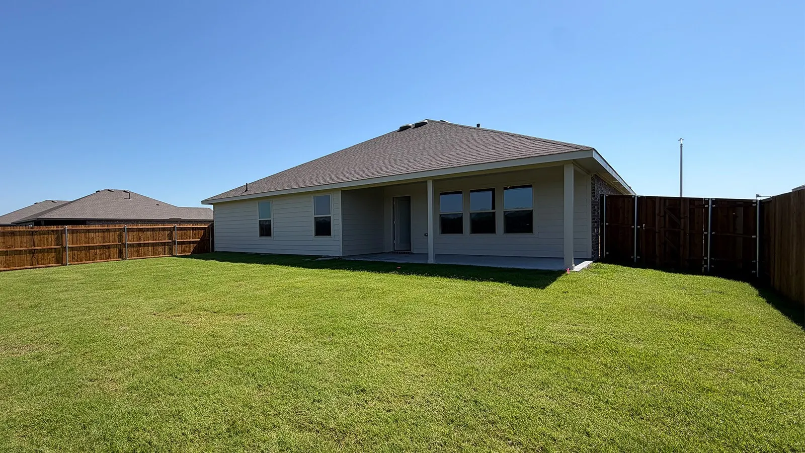Expansive fenced backyard featuring a covered patio, neutral-toned siding, a dark shingle roof, and multiple windows