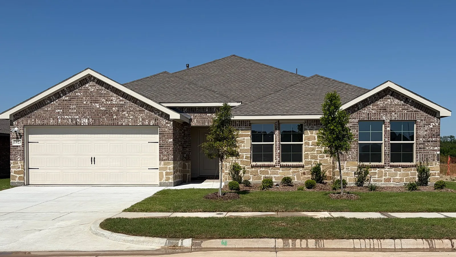 Brick and stone veneer exterior featuring a two-car garage with carriage-style doors, dark framed windows, and a shingled roof