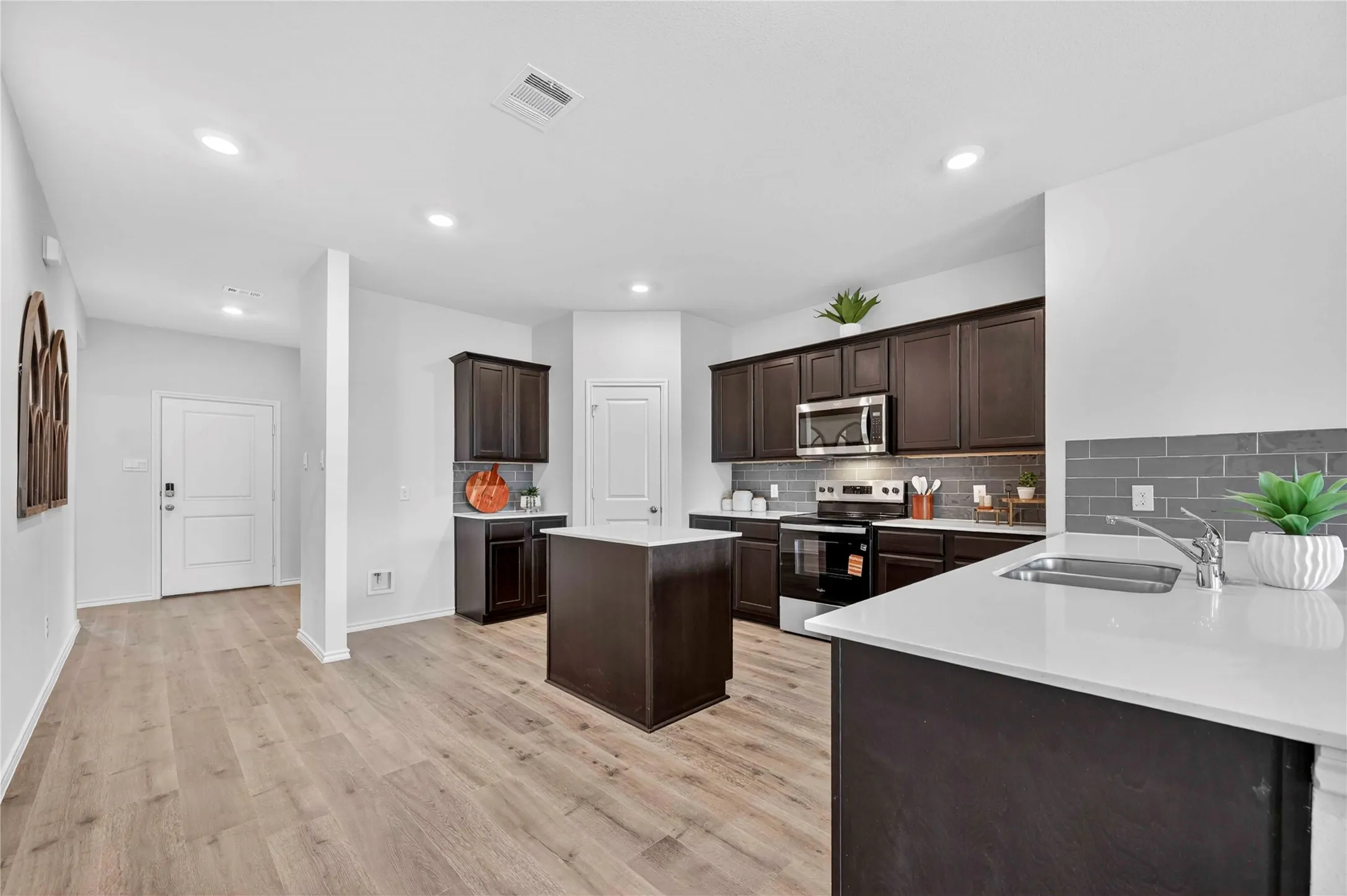 Kitchen featuring dark wood cabinetry, stainless steel appliances, a center island with a light-toned countertop, and light wood-finish flooring