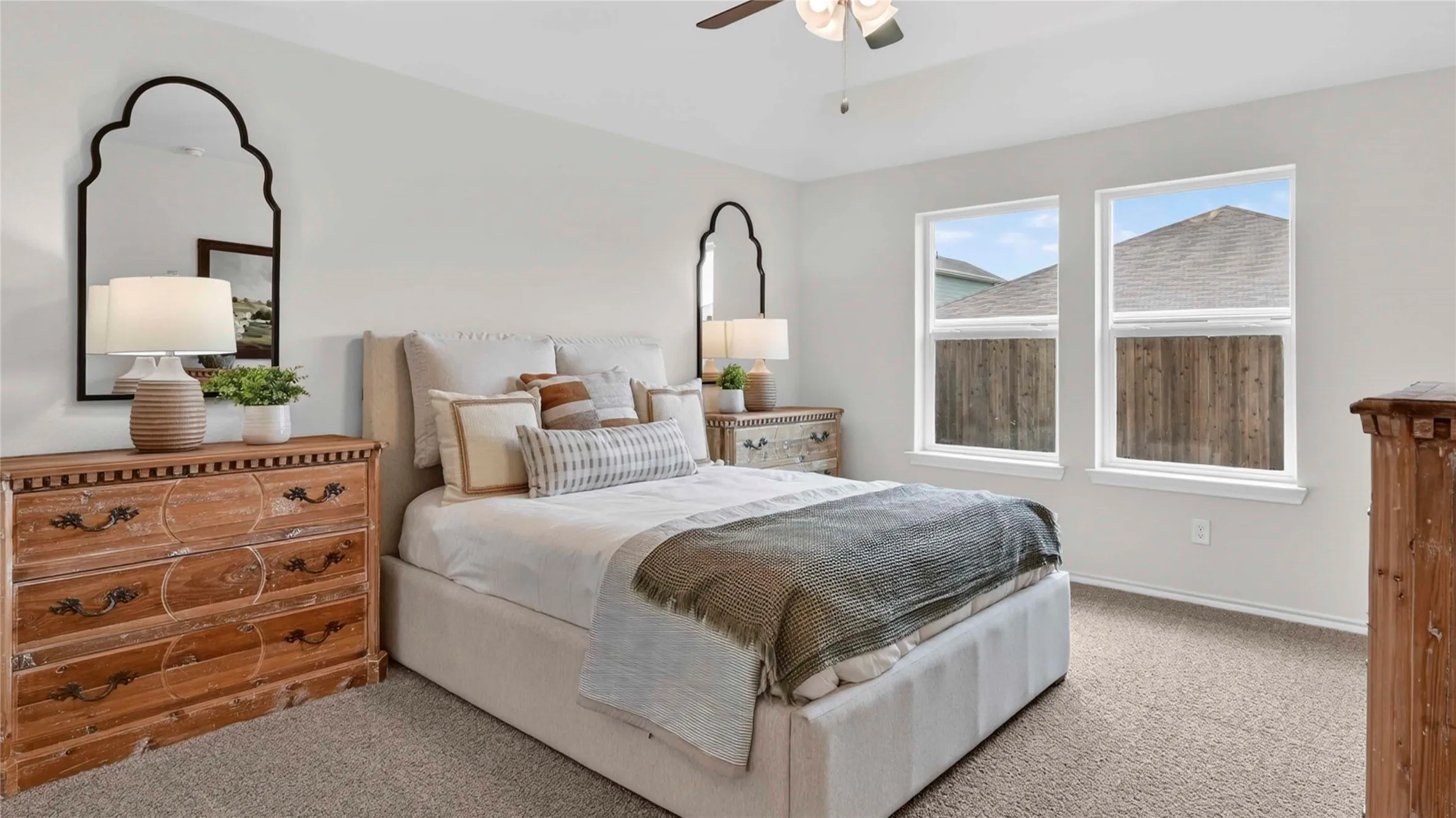 Carpeted bedroom featuring two large windows, a ceiling fan with integrated lighting, and neutral wall tones