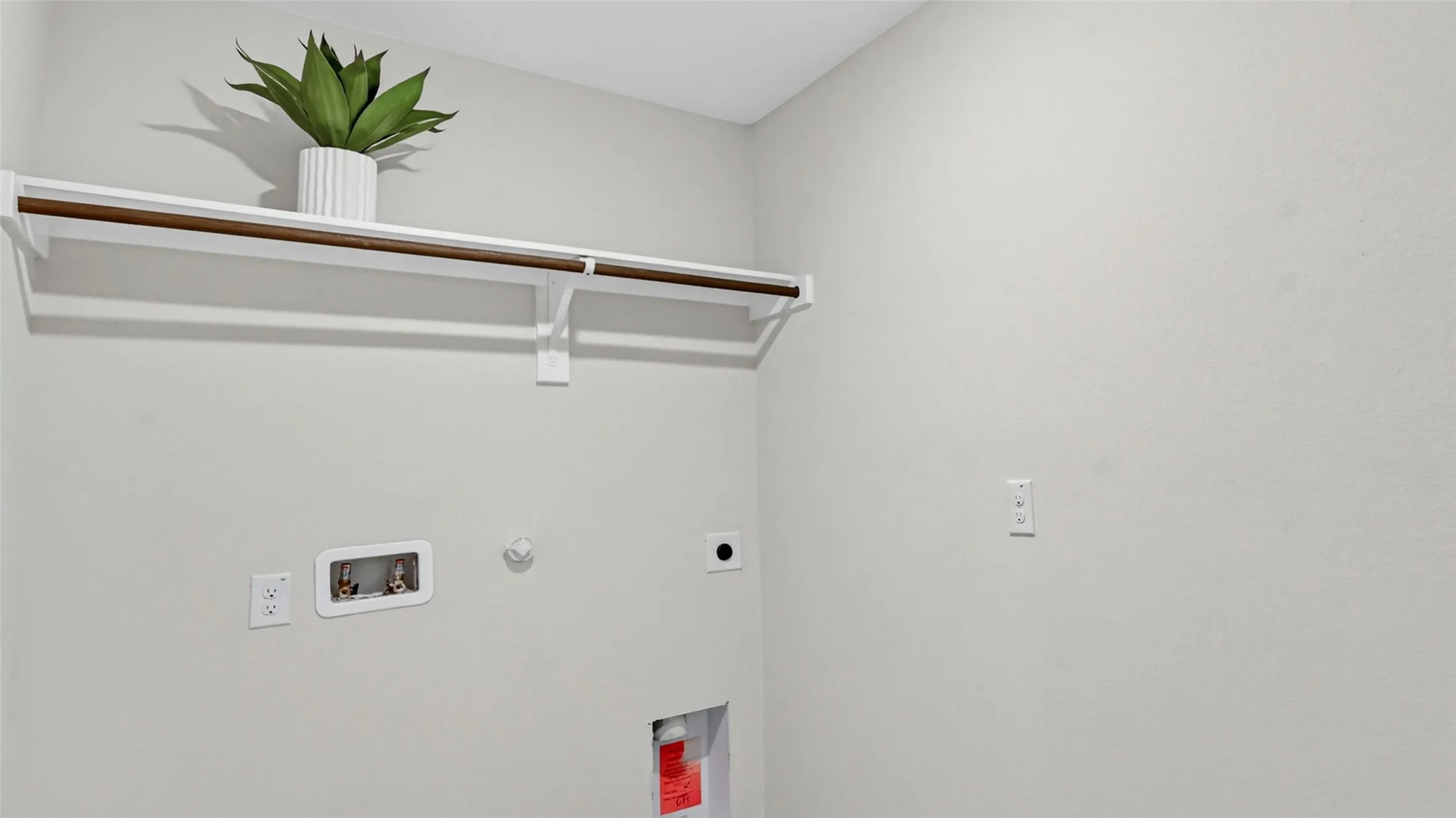 Utility area featuring a mounted shelf with a hanging rod, water hookups, and electrical outlets