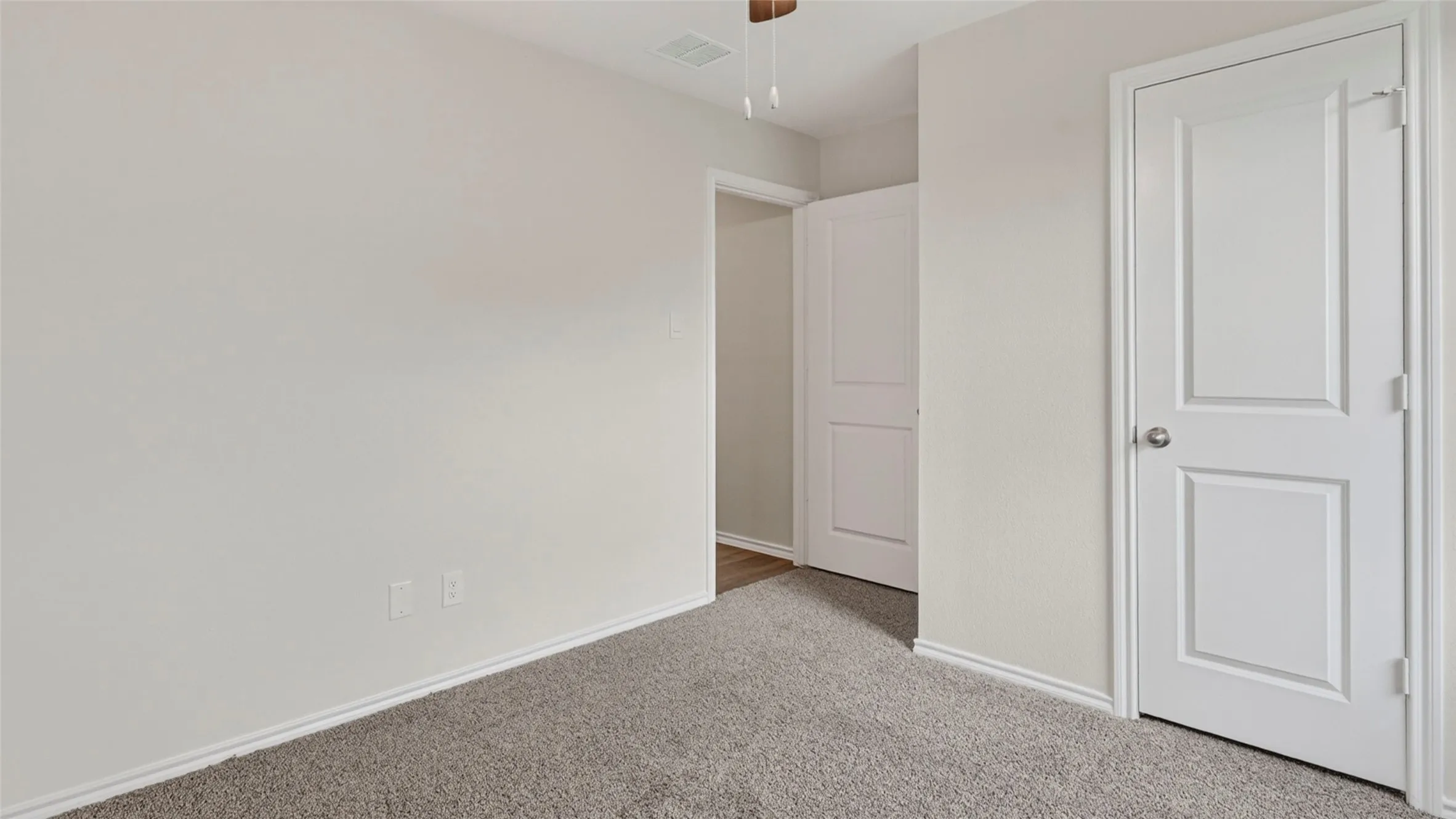 Carpeted room featuring light gray walls, white trim, two paneled interior doors, and a ceiling fan