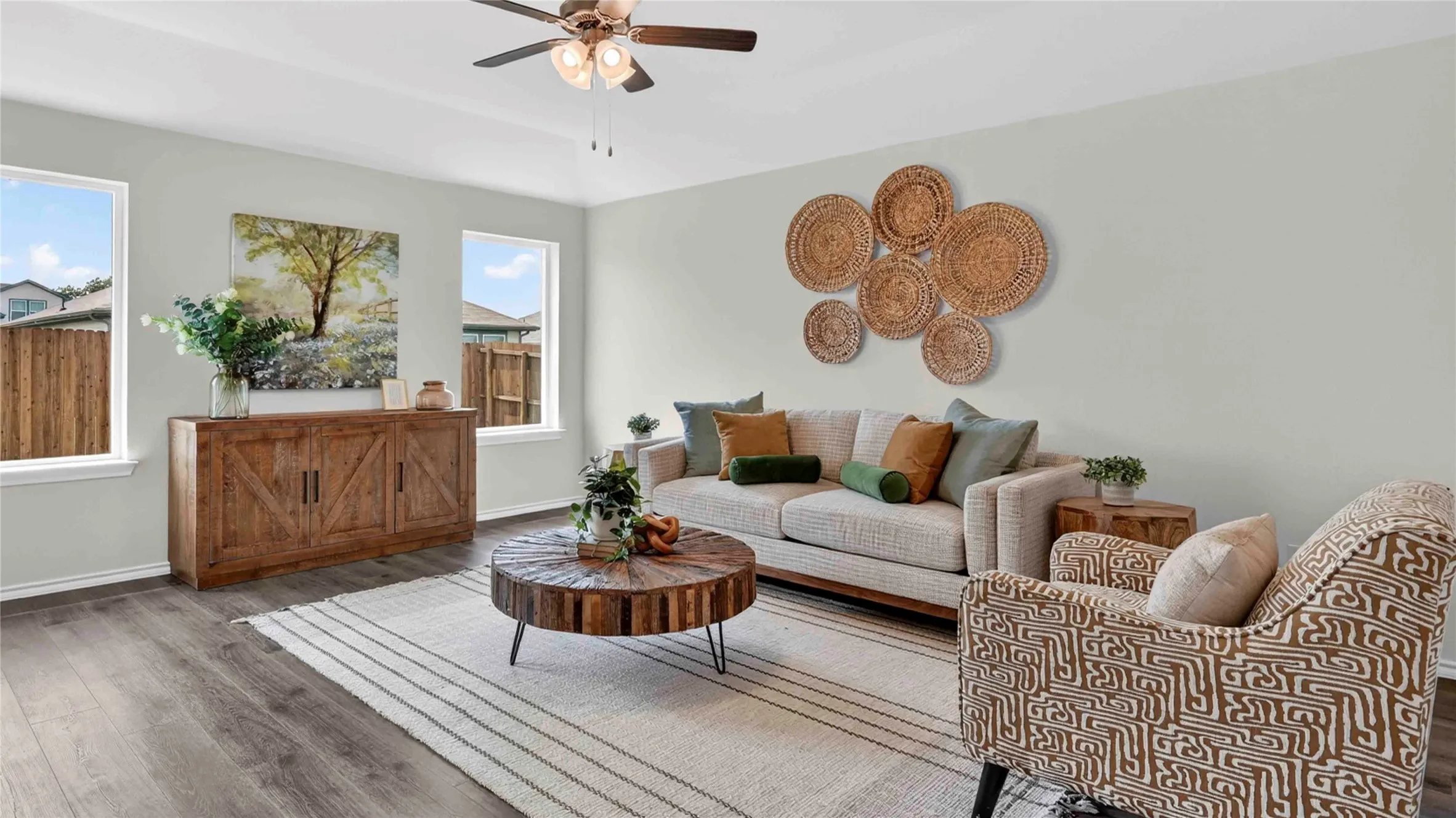 Spacious living area featuring wood-finish flooring, light neutral wall tones, and a ceiling fan with integrated lighting