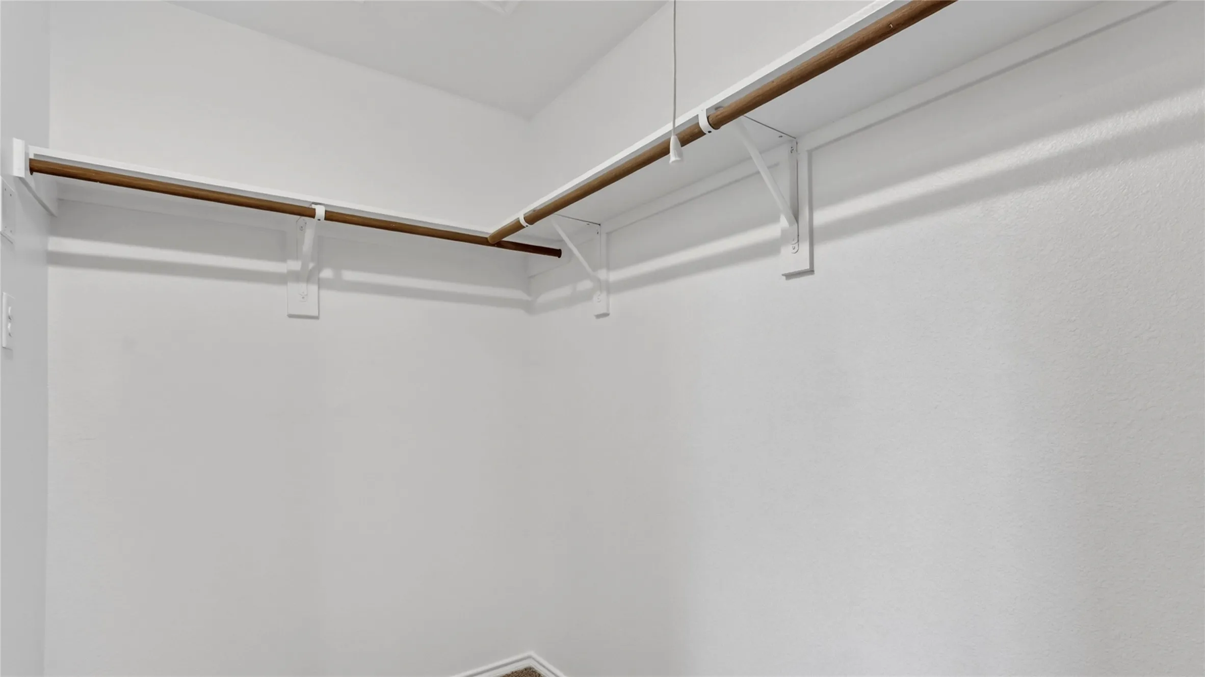 Walk-in closet featuring white painted walls, wood-finish hanging rods, and white shelf supports