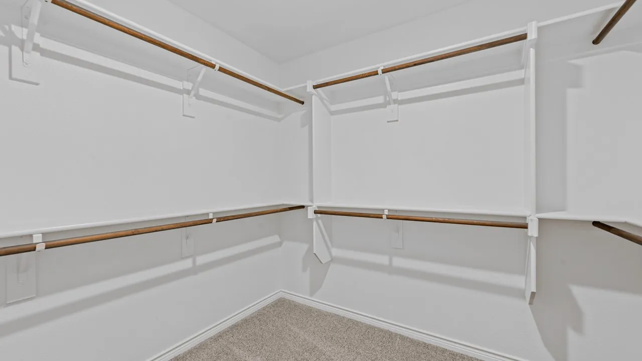 Walk-in closet featuring white walls, carpeted flooring, and multiple wooden hanging rods