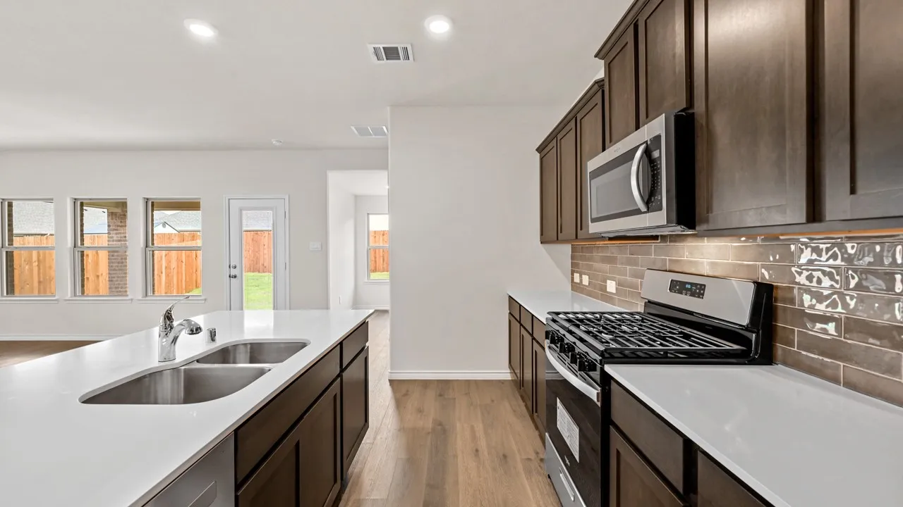 Kitchen featuring wood-finish flooring, dark wood cabinetry, white countertops, stainless steel appliances, and a brown tiled backsplash