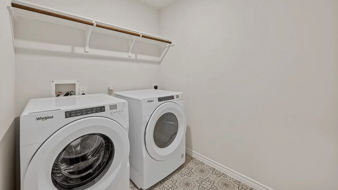 Utility area featuring a patterned tile floor, a built-in shelf with a hanging rod, and white baseboards