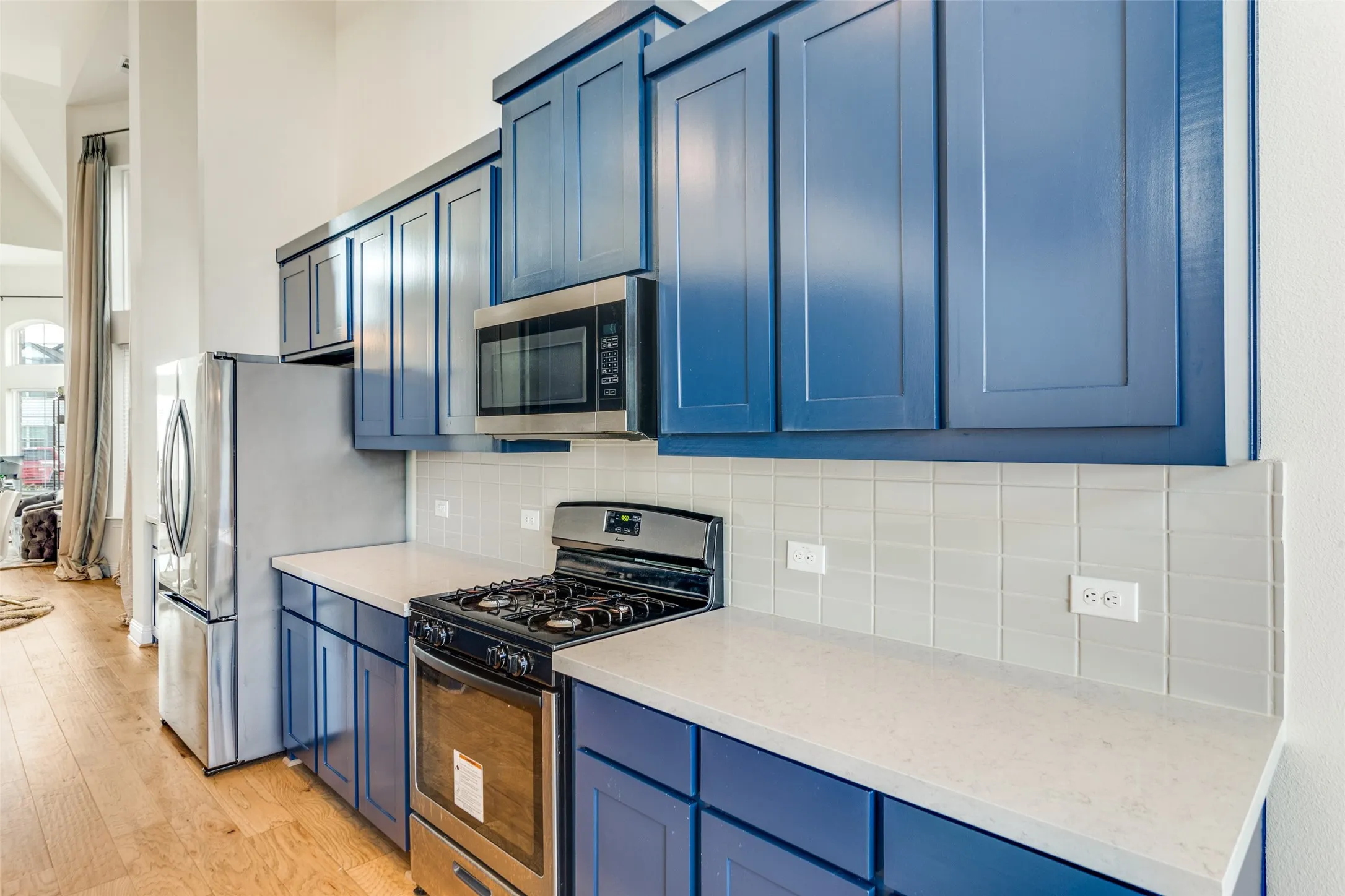 Kitchen featuring stainless steel appliances, blue cabinetry, light wood-style floors, decorative backsplash, and light stone countertops