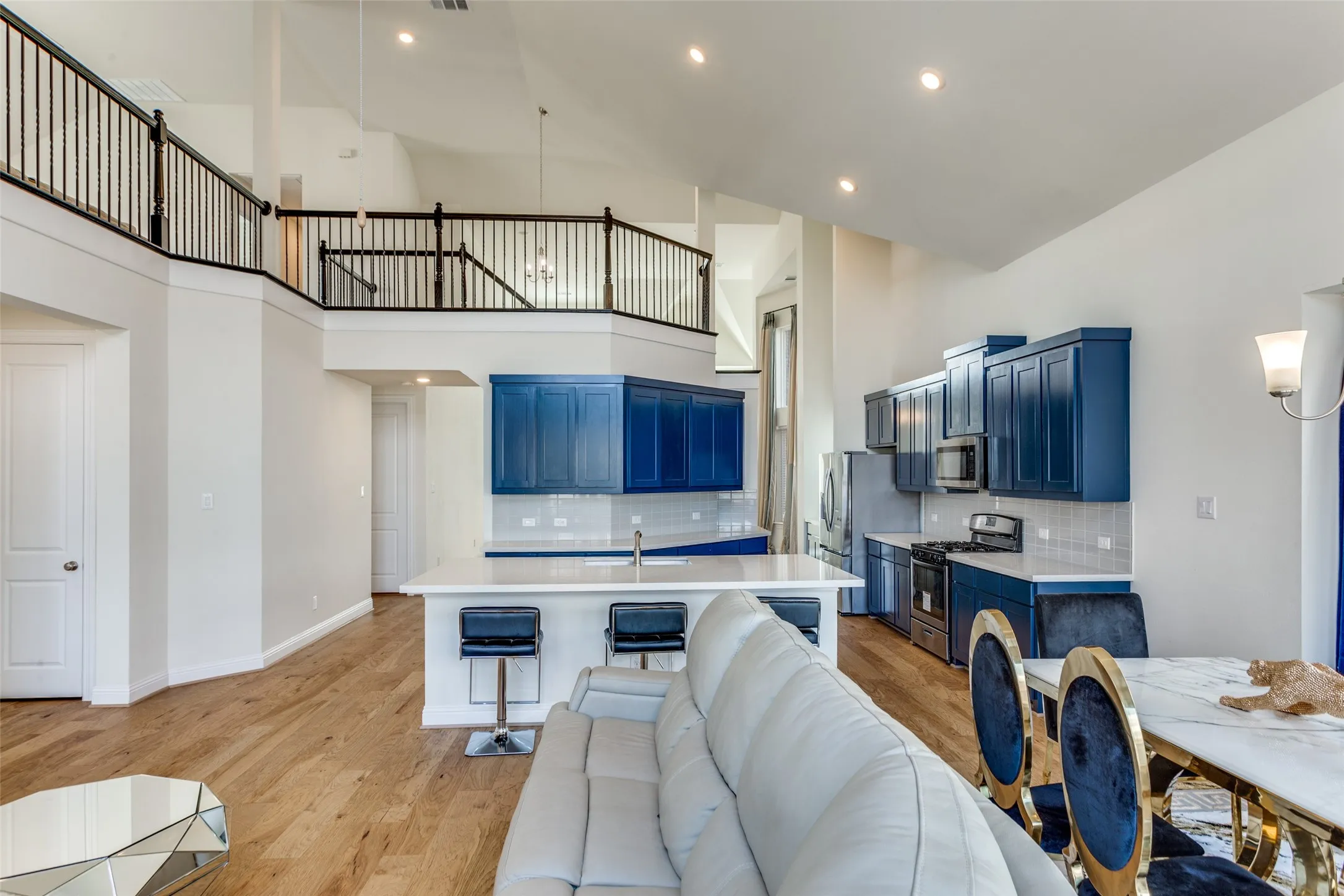 Kitchen with blue cabinetry, light countertops, light wood-style flooring, stainless steel appliances, and a high ceiling