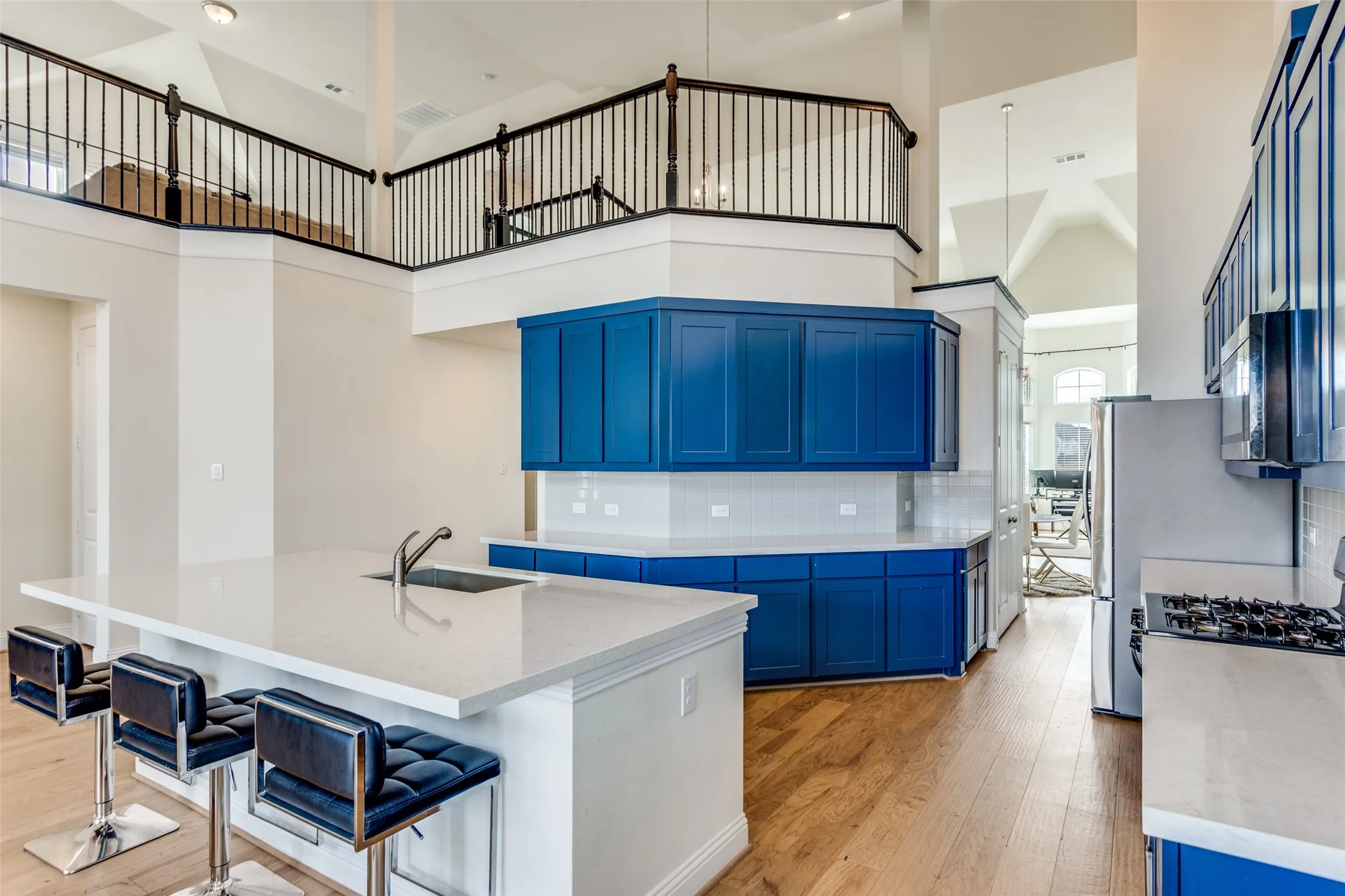 Kitchen featuring blue cabinetry, a kitchen bar, a center island with sink, light stone countertops, and light wood-style flooring