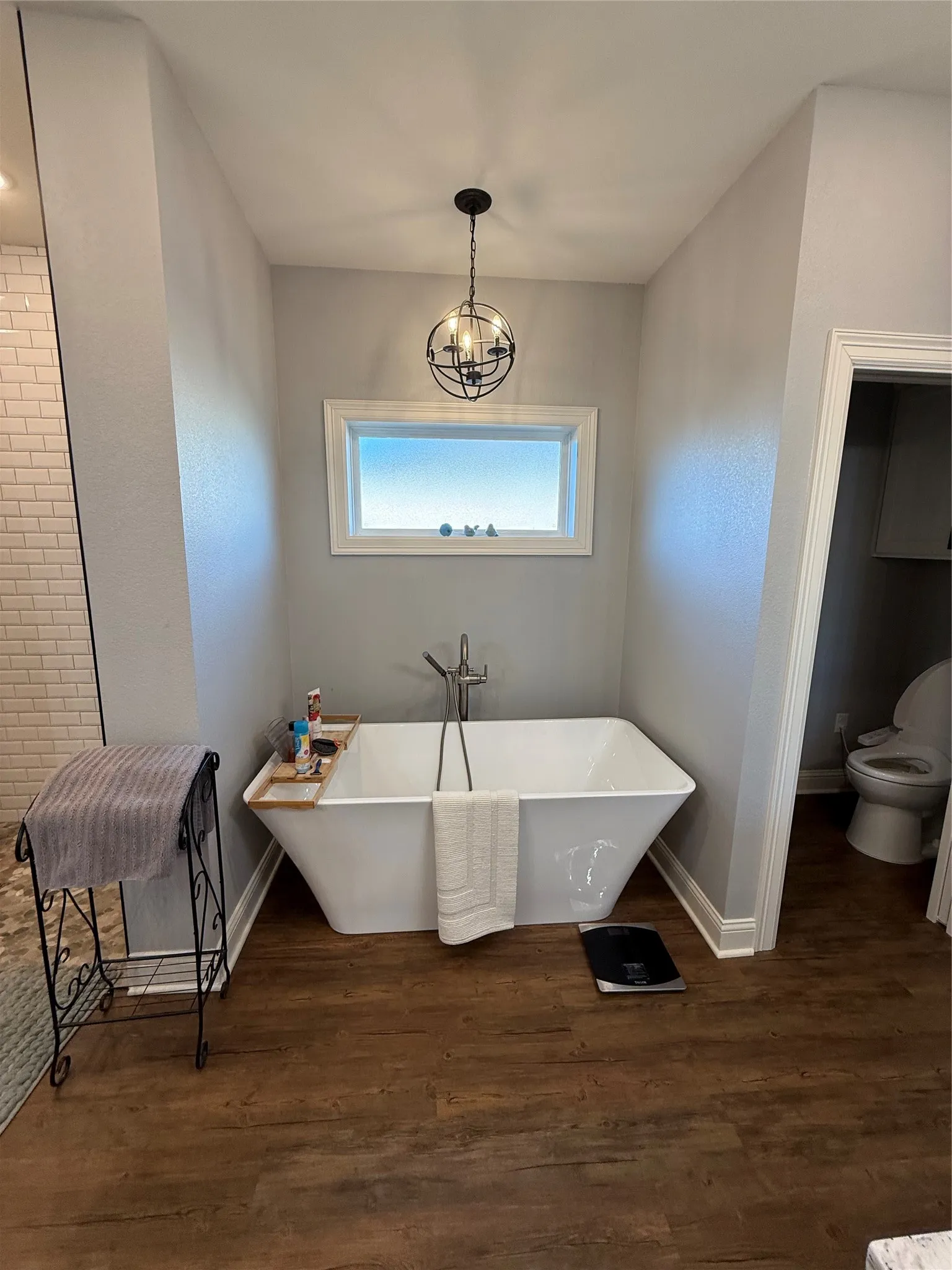 Bathroom featuring toilet, a freestanding tub, wood finished floors, and baseboards