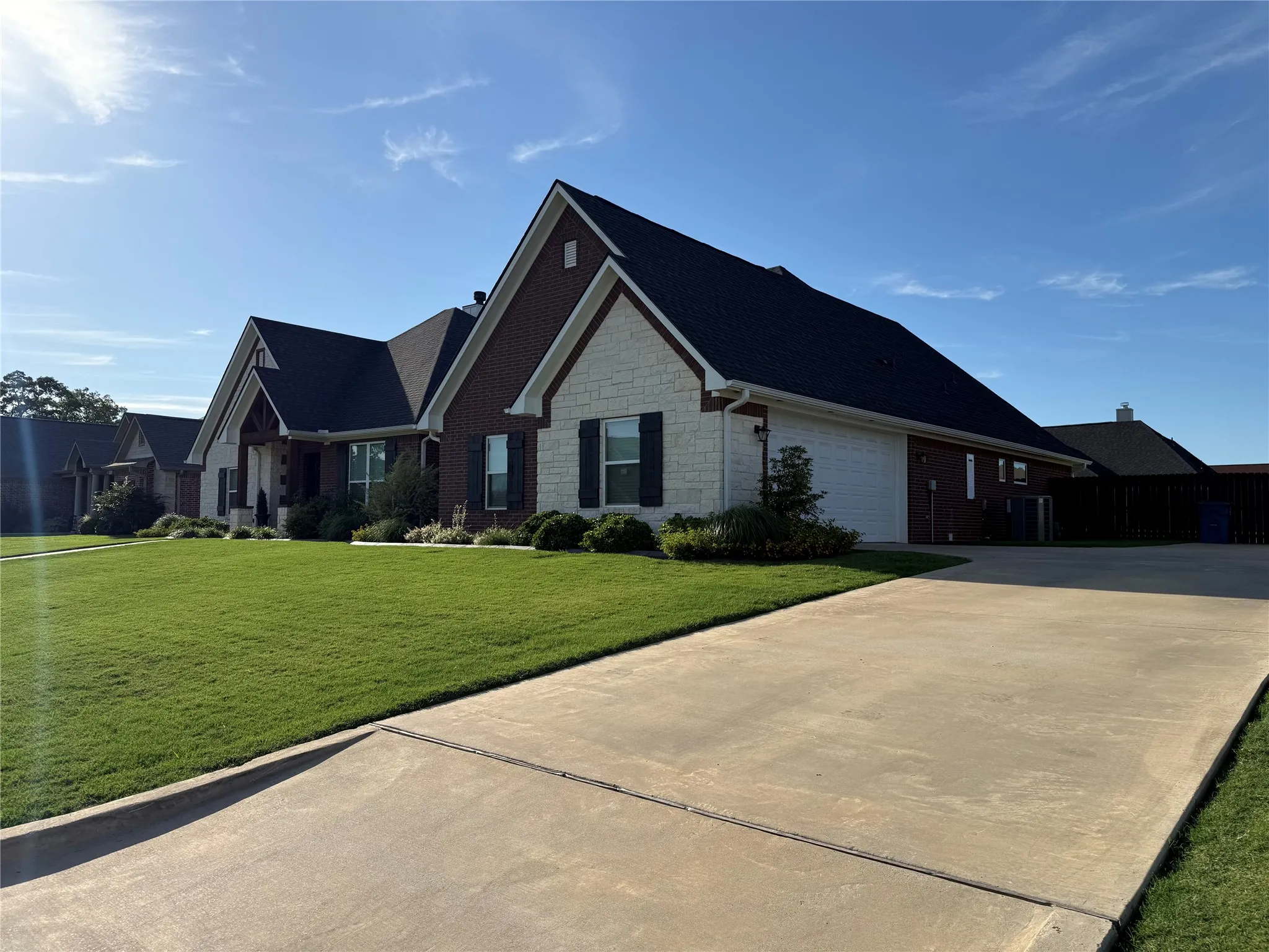 View of front facade with stone siding, an attached garage, concrete driveway, central air condition unit, and brick siding