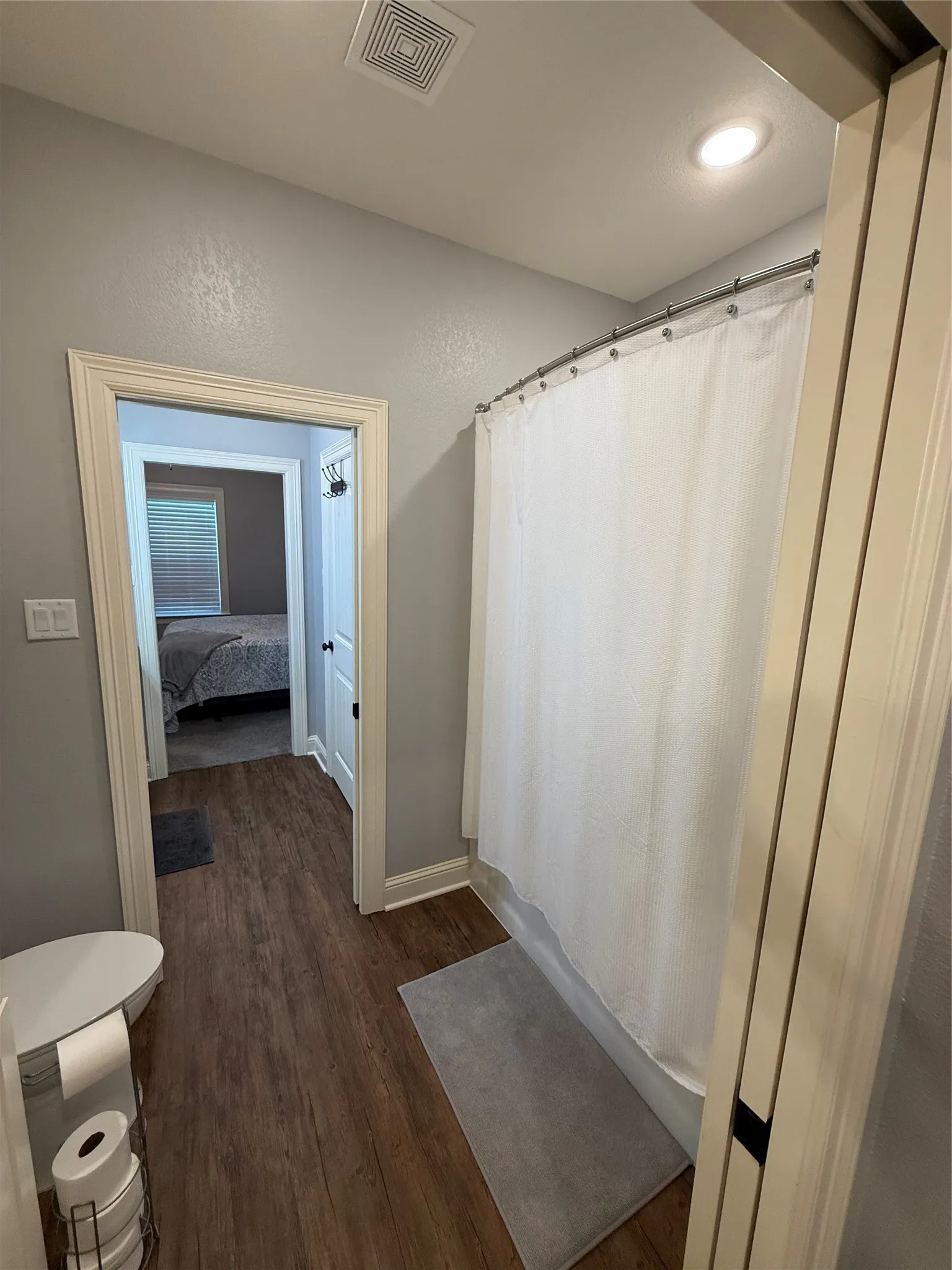 Full bath featuring wood finished floors, toilet, baseboards, and a shower with curtain