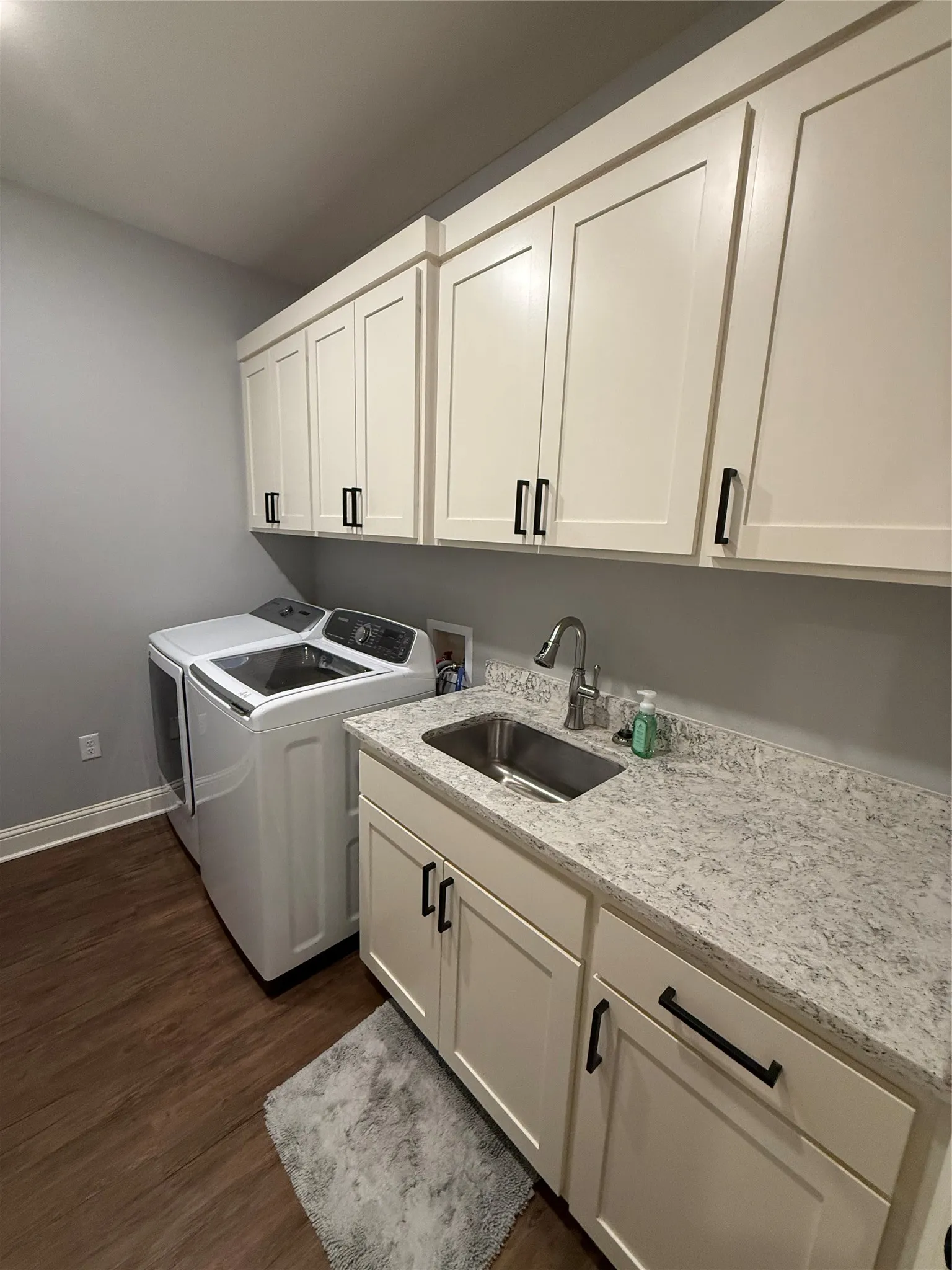 Washroom featuring cabinet space, washer and dryer, dark wood-type flooring, and baseboards