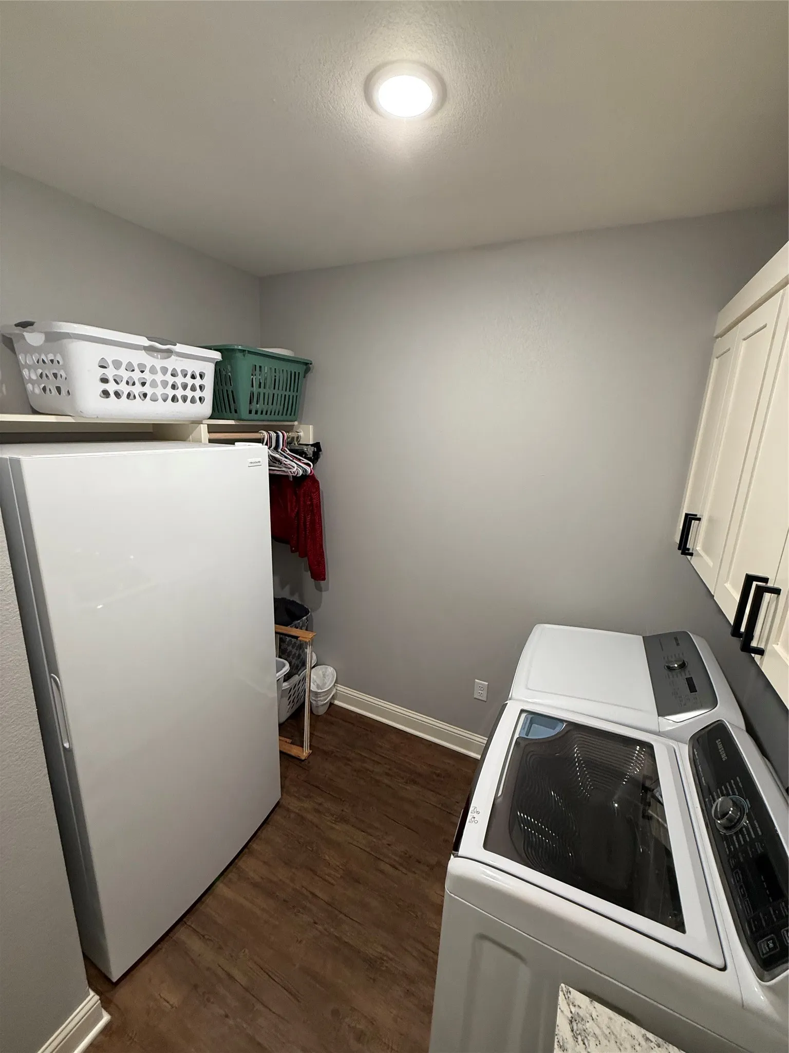 Washroom featuring cabinet space, washing machine and clothes dryer, baseboards, and dark wood-style flooring