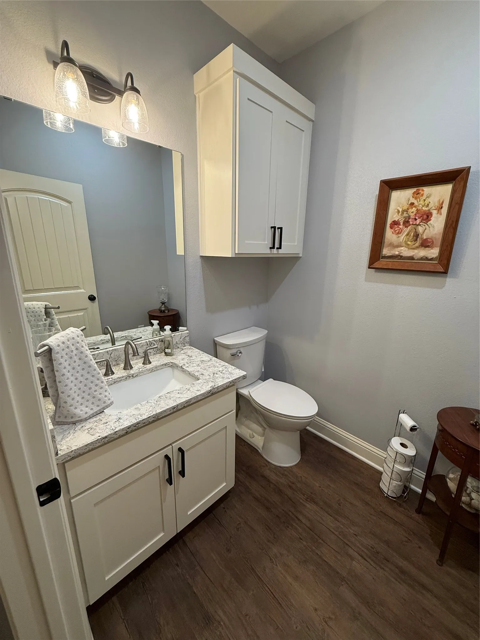 Half bathroom with wood finished floors, baseboards, vanity, and toilet