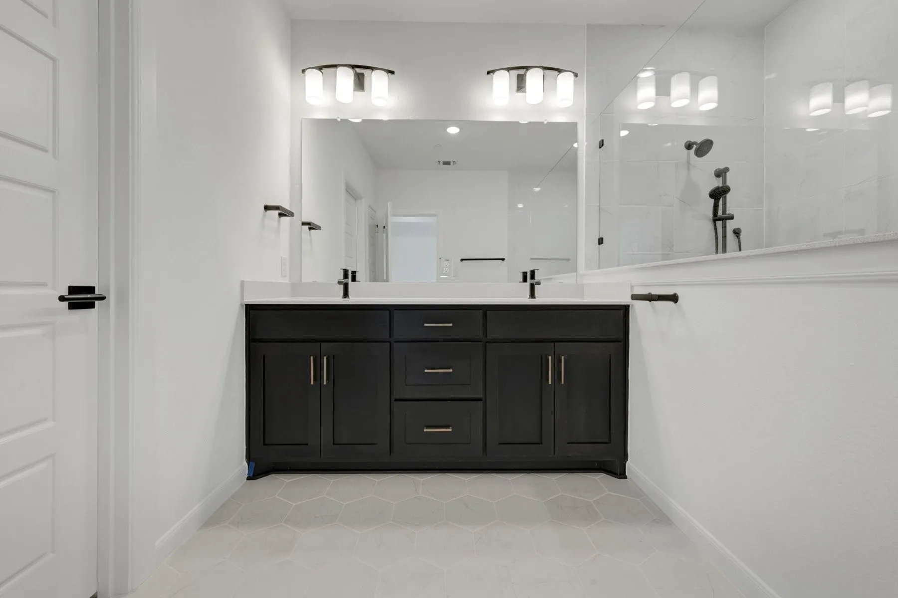 Dual vanity with black cabinetry, white countertops, hexagon tile flooring, and a glass-enclosed shower with black fixtures