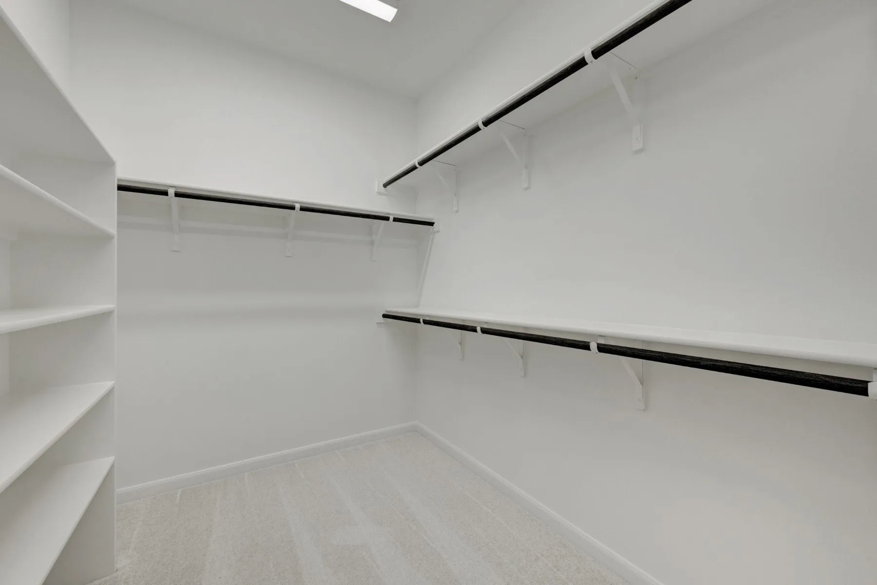 Spacious walk-in closet featuring built-in shelving, multiple hanging rods, light-colored carpet, and recessed ceiling lighting