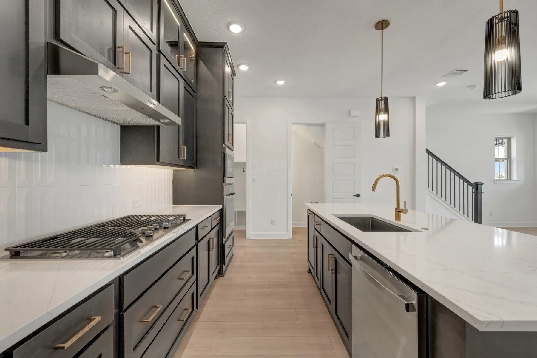 Modern kitchen featuring a gas cooktop, stainless steel hood, quartz countertops, a large island with an undermount sink, and dark cabinetry with brass hardware