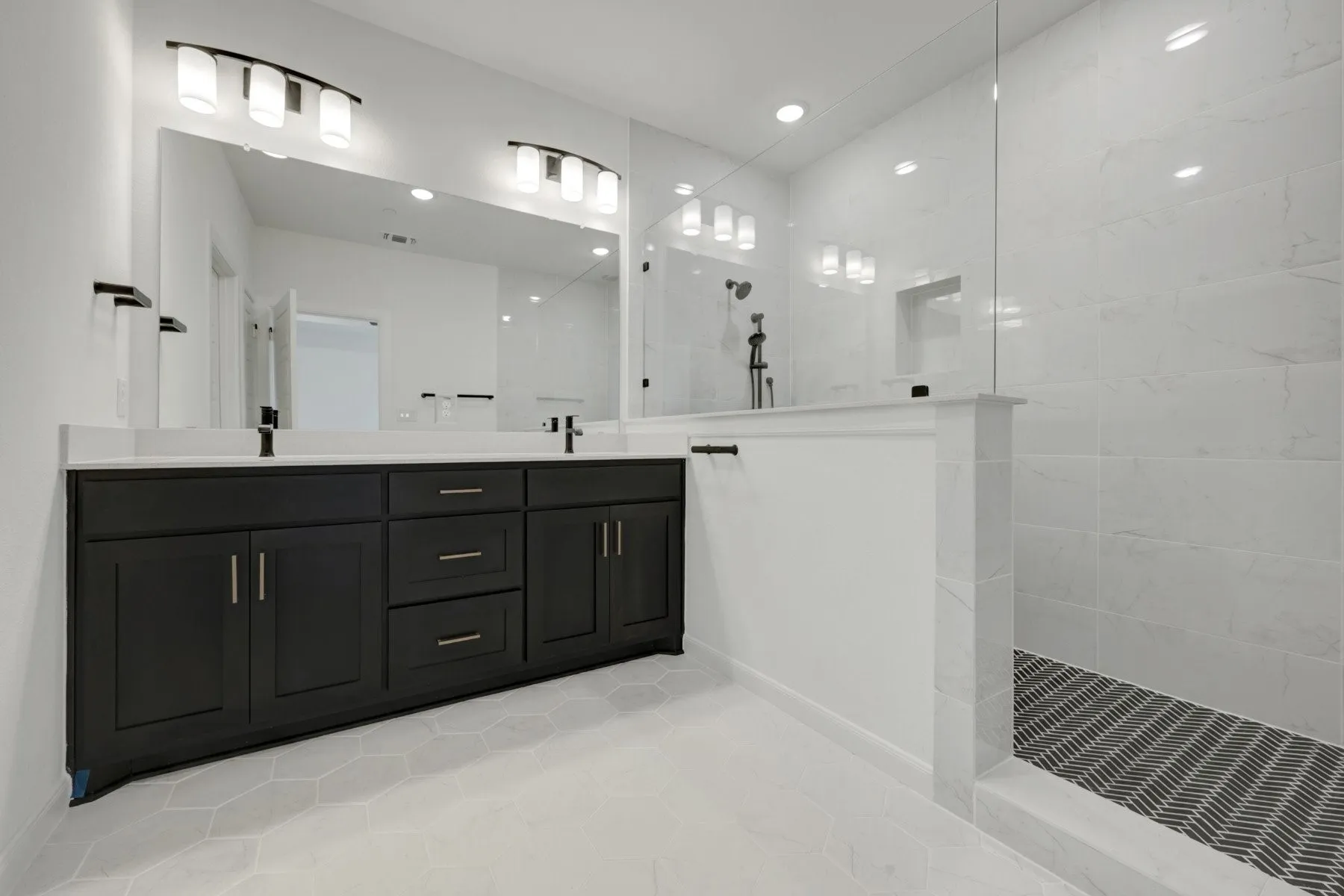 Contemporary bathroom featuring a dark wood double vanity with white countertops, expansive wall-mounted mirror, and a spacious walk-in shower with white tile walls and a patterned floor
