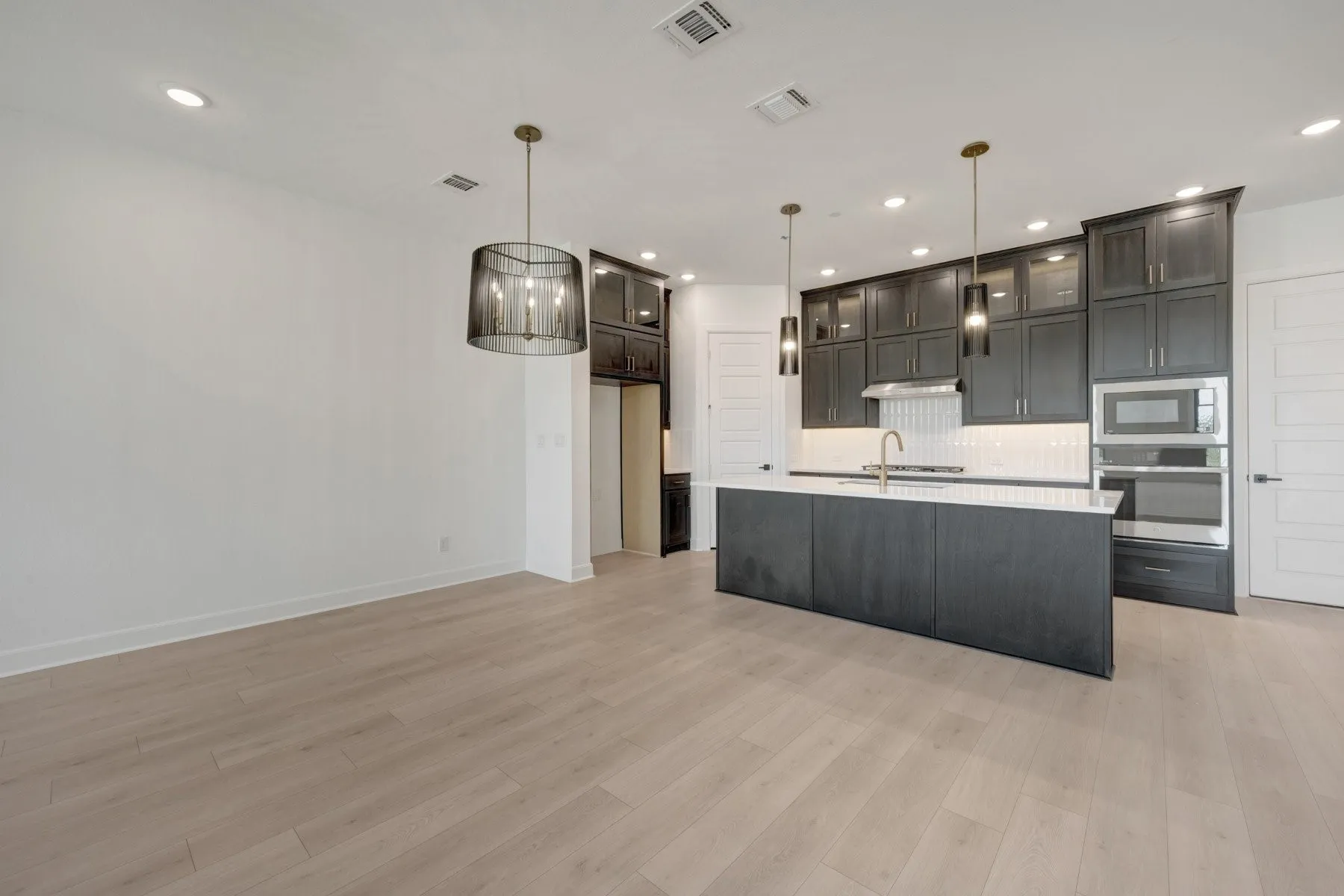 Modern kitchen featuring an island with a white countertop, dark cabinetry, and integrated stainless steel appliances
