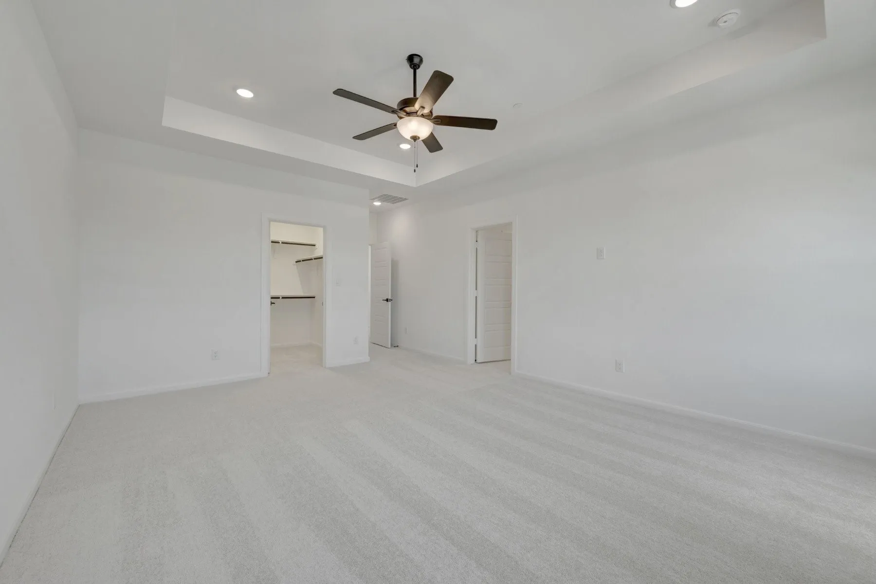Spacious room featuring light-toned carpet, a tray ceiling with recessed lighting, and a dark-finished ceiling fan