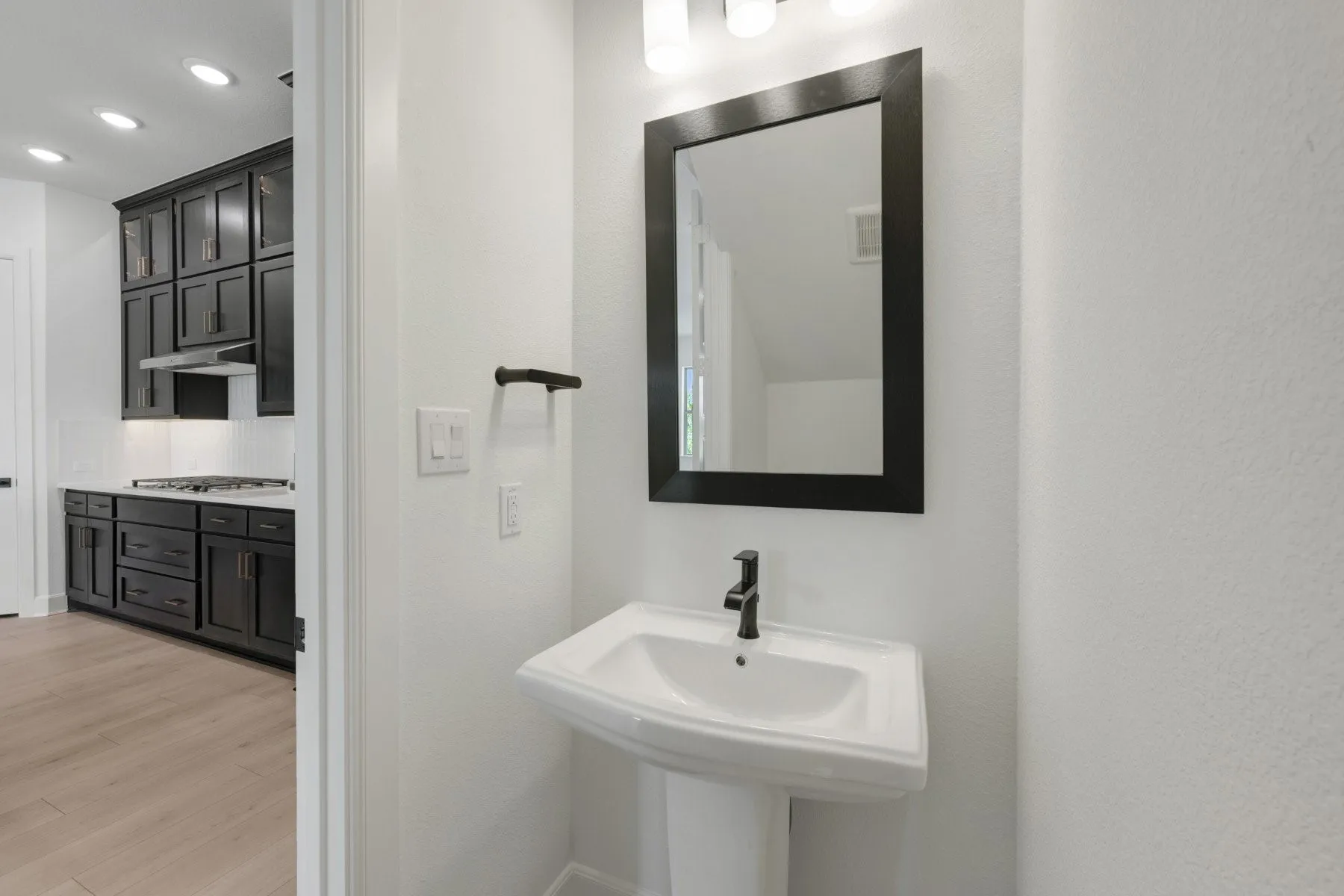 Pedestal sink with matte black faucet, framed mirror, and contemporary light fixture