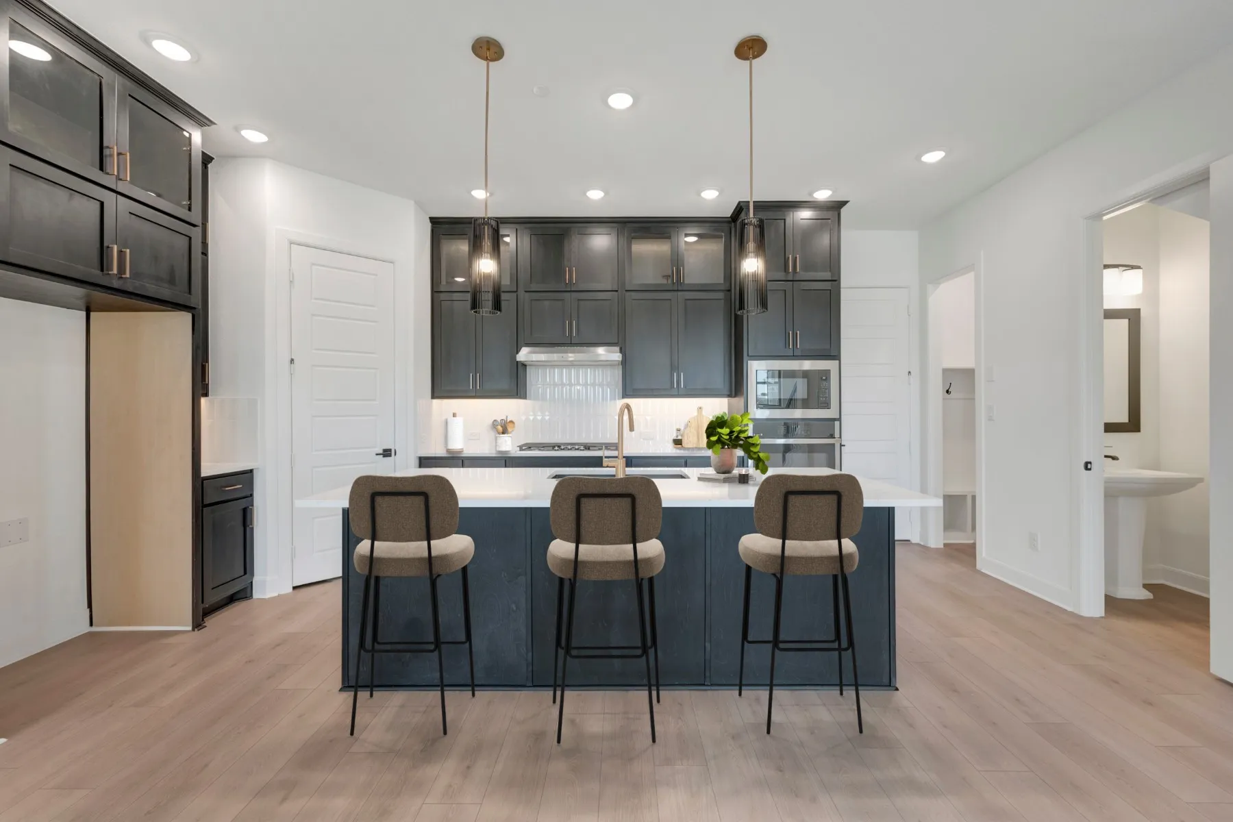 Modern kitchen featuring a central island with seating, dark shaker cabinetry, stainless steel appliances, and wood-finish flooring