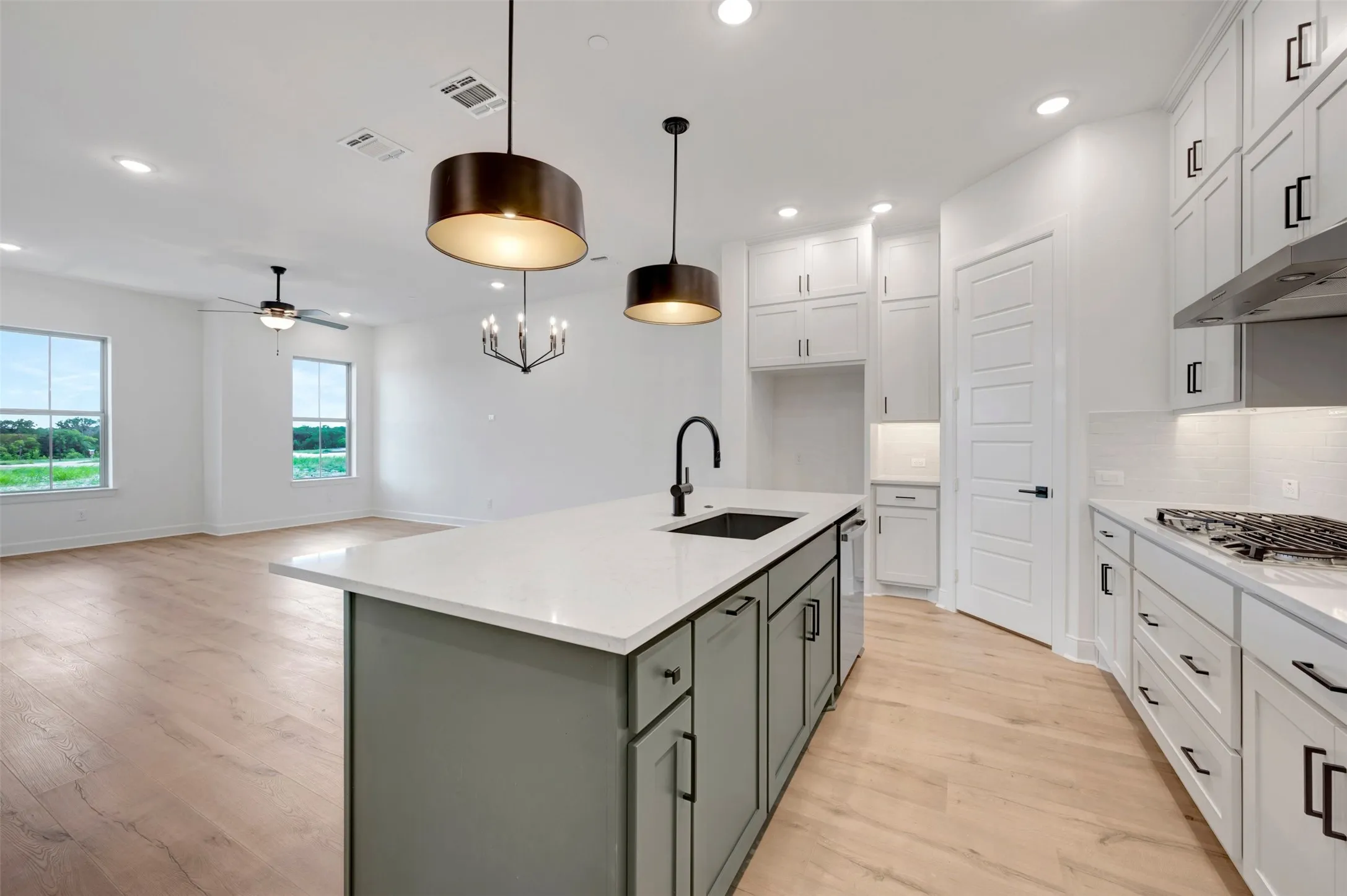 Open-concept kitchen featuring an island with a built-in sink, white countertops, a gas range with an overhead vent, and wood-finish flooring throughout