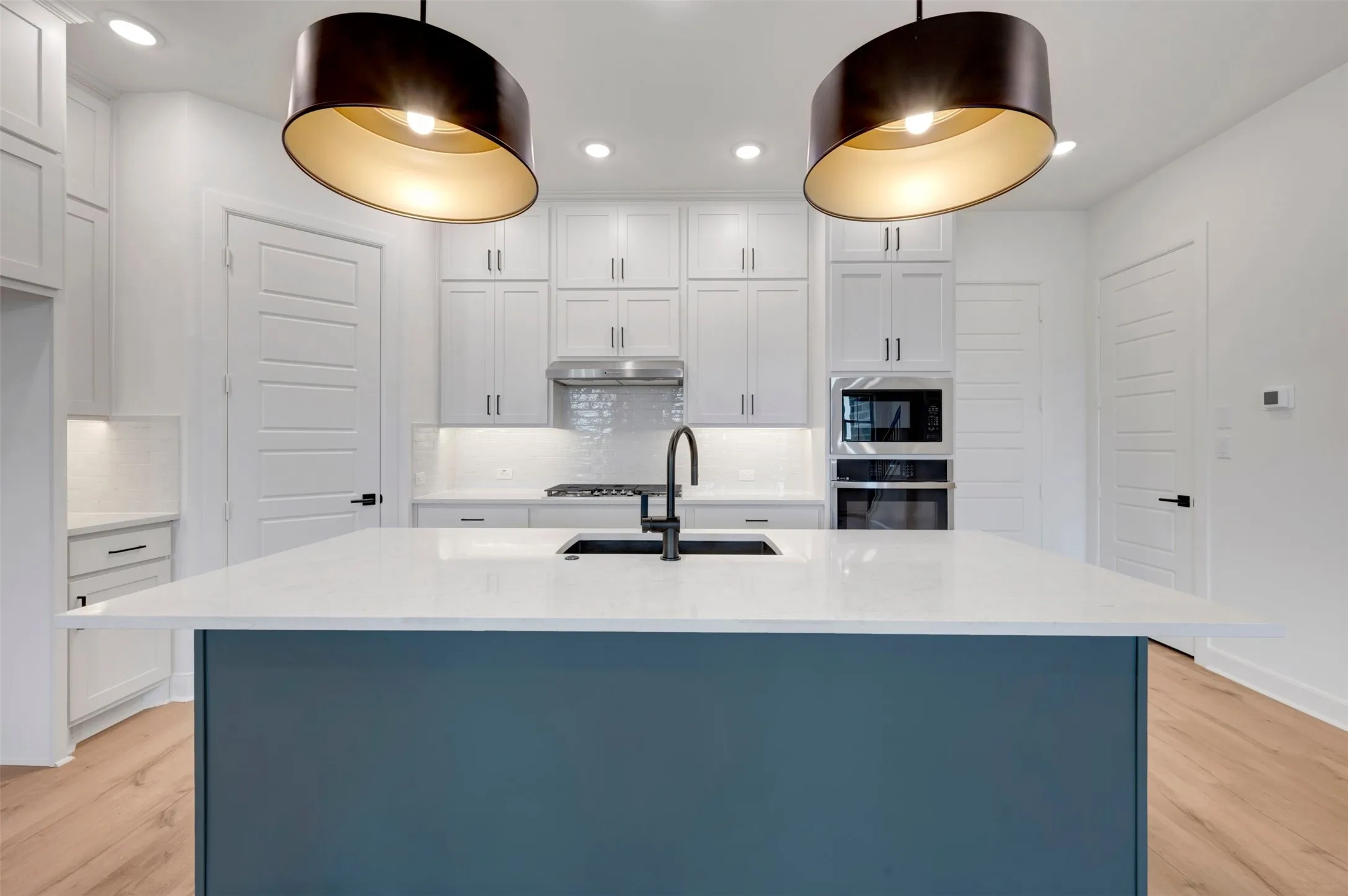 Kitchen featuring a large island with a white countertop and blue-finish base, dual contemporary pendant lighting, white shaker cabinetry, stainless steel appliances, and wood-finish flooring