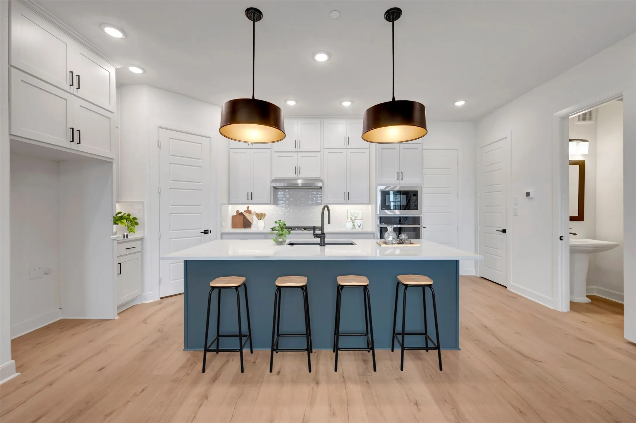 Modern kitchen featuring a blue island with a white countertop, two pendant lights, recessed lighting, and wood-finish flooring