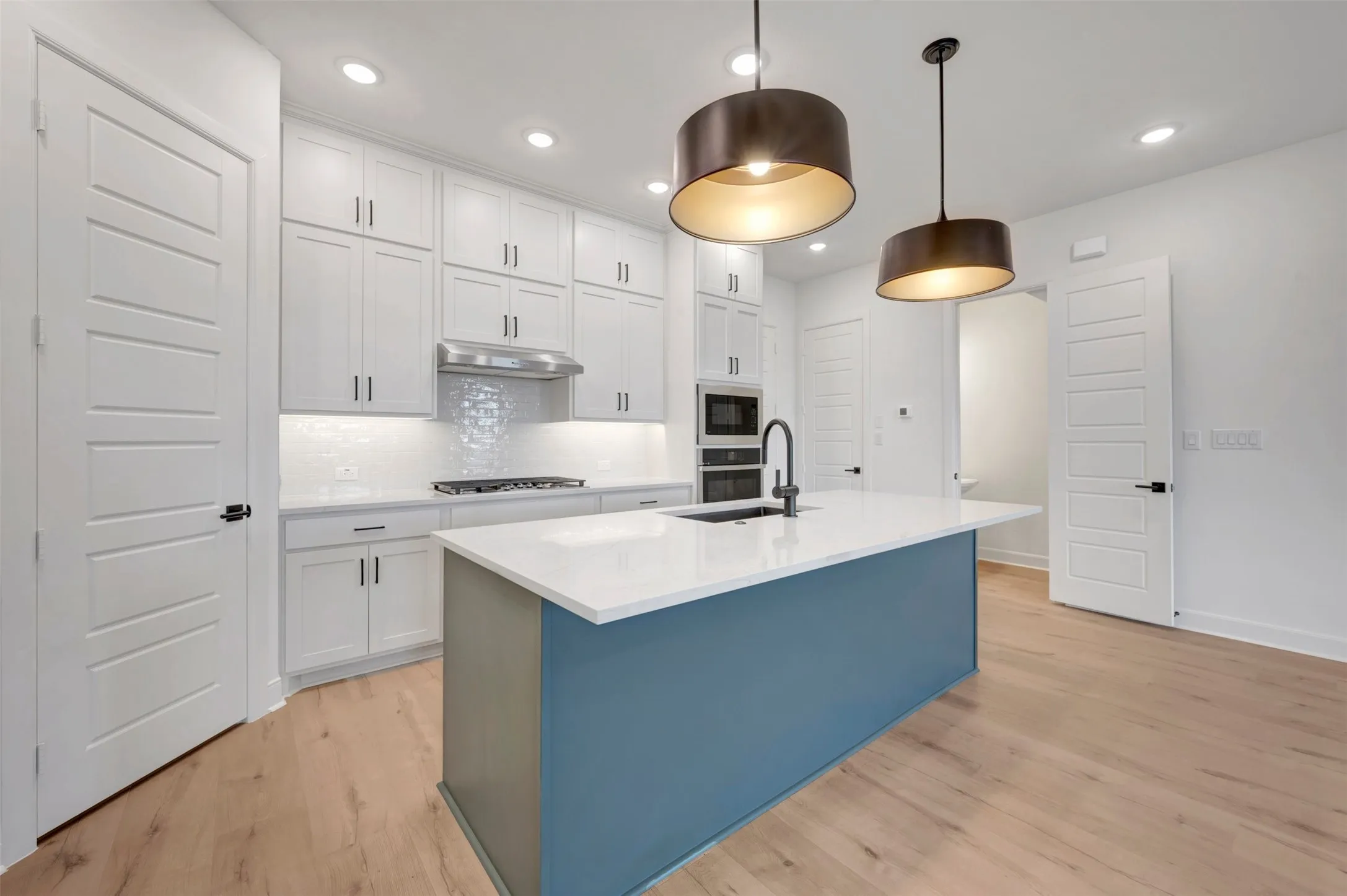 Contemporary kitchen featuring a blue-toned island with a white countertop and dark pendant lighting
