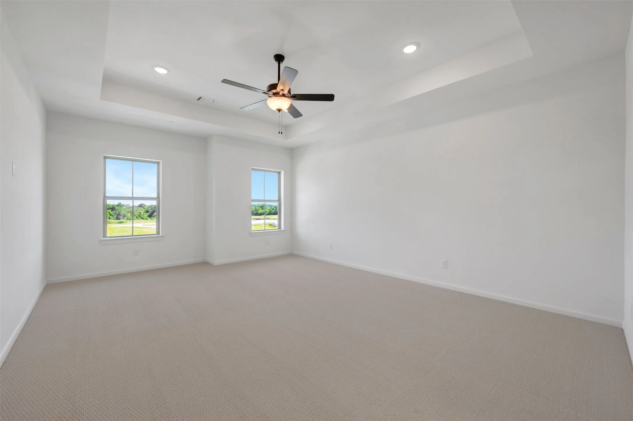 Spacious interior room featuring a tray ceiling with recessed lighting and a ceiling fan