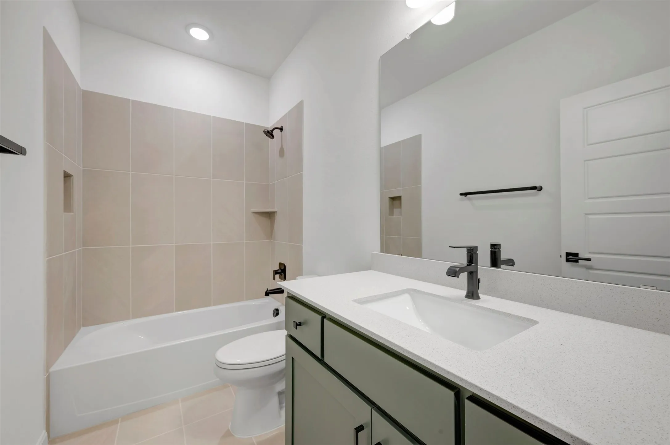 Bathroom featuring a built-in tub with tile surround, a single vanity with a quartz countertop, an integrated sink, and matte black fixtures