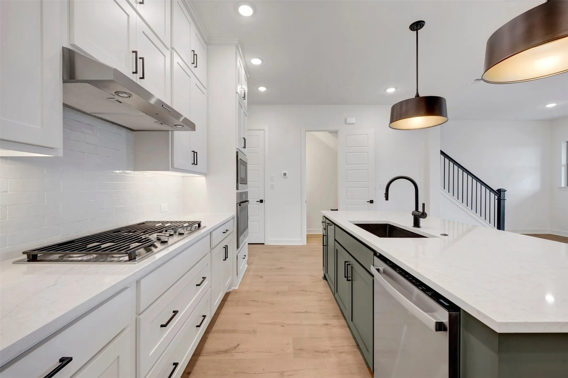 Contemporary kitchen featuring a gas range, stainless steel appliances, white cabinetry with dark hardware, a center island with a sink, and wood-finish flooring