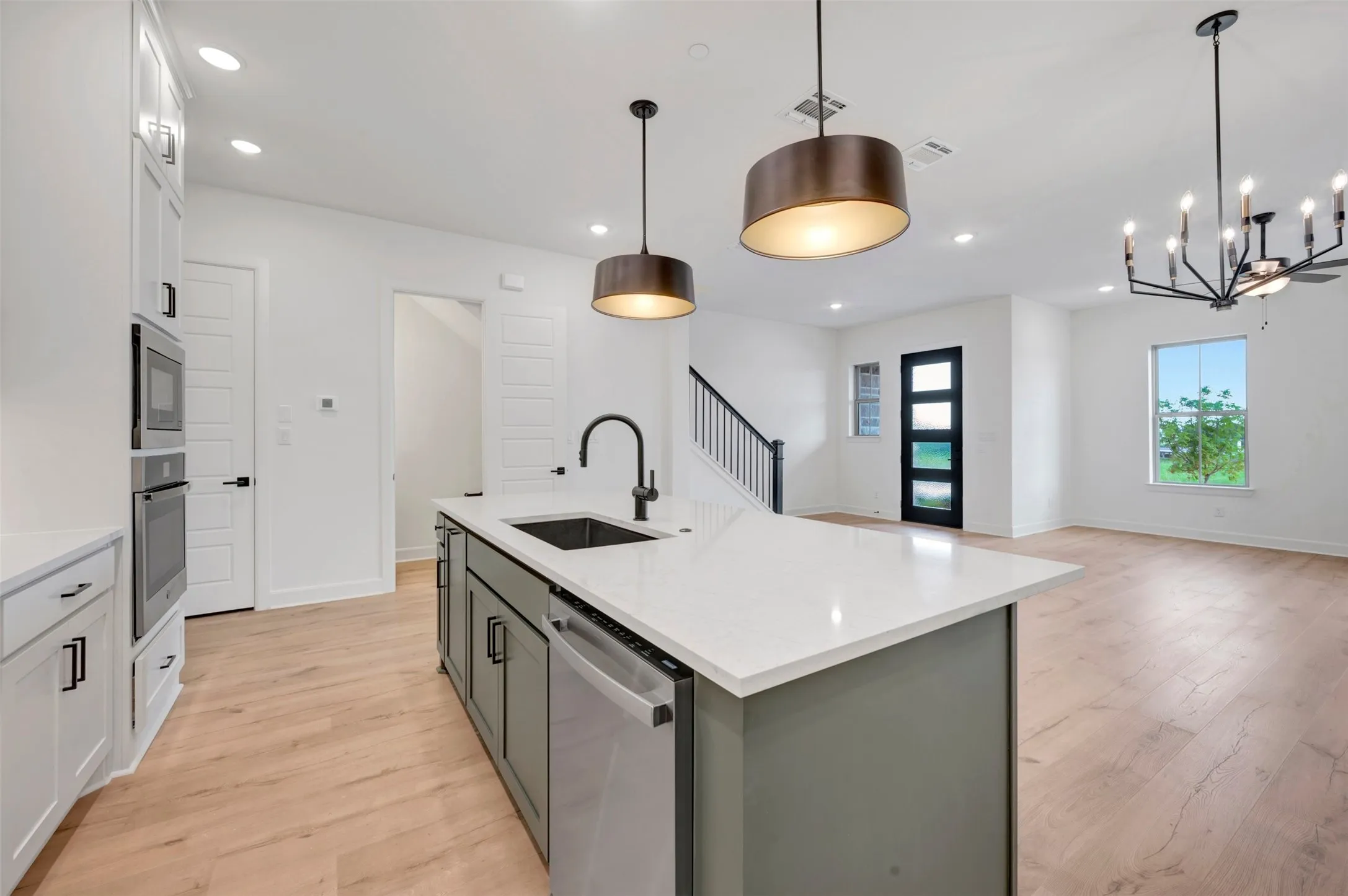 Open-concept kitchen featuring a spacious island with a countertop and built-in sink, stainless steel appliances, white cabinetry, and wood-finish flooring