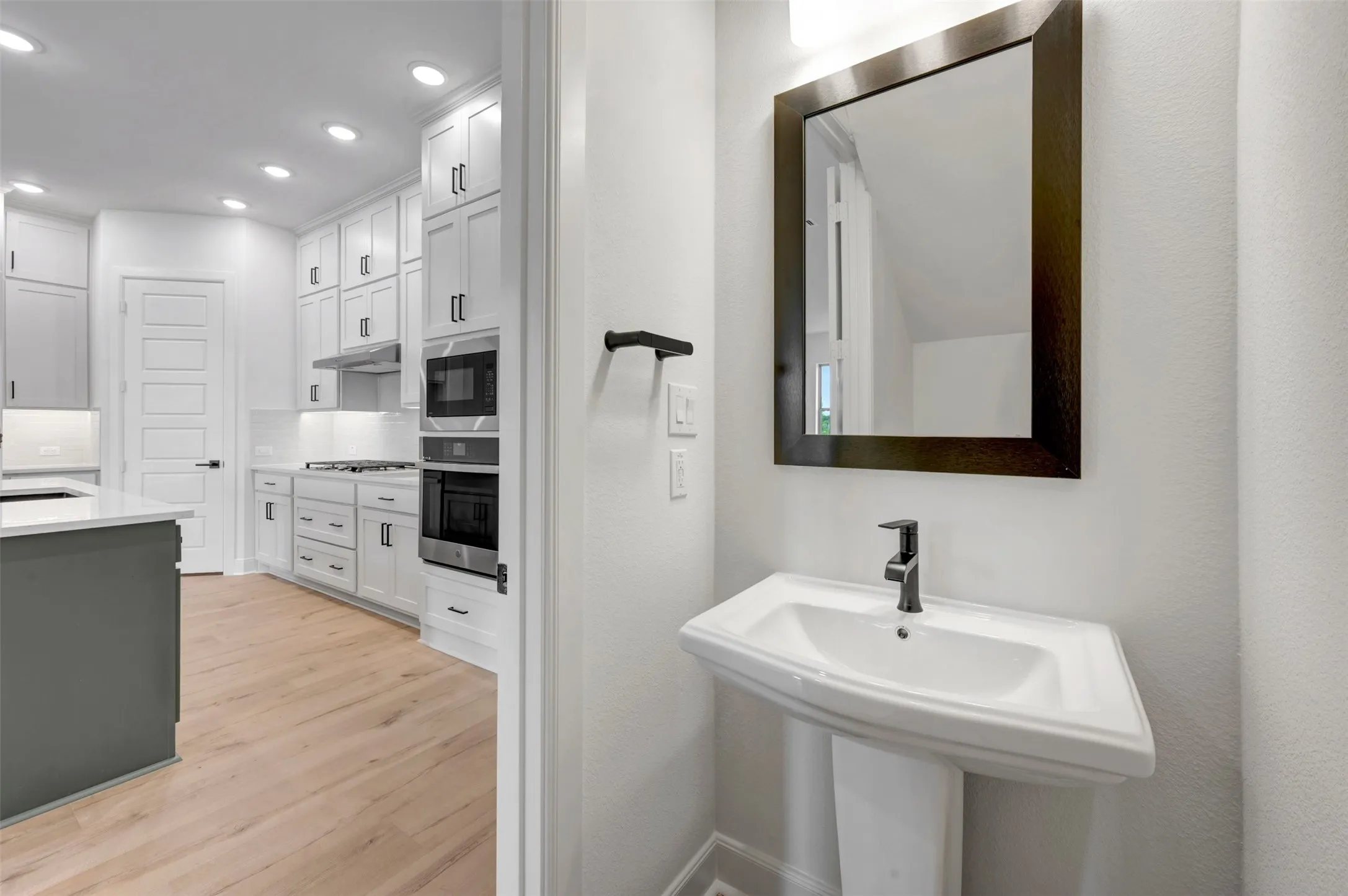 Pedestal sink with a dark framed mirror and wall-mounted light fixture