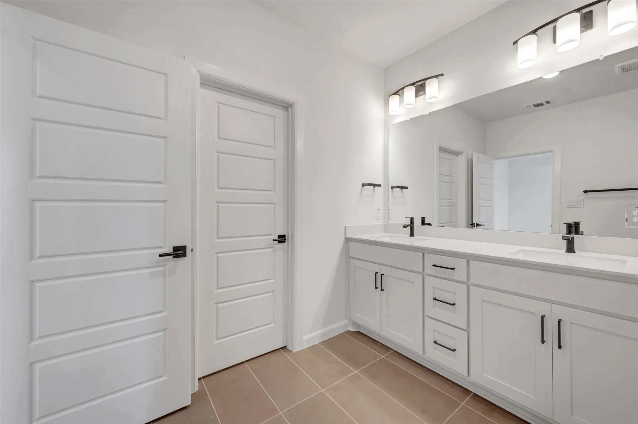 Double vanity featuring white cabinetry, integrated sinks, black hardware, and an expansive wall mirror