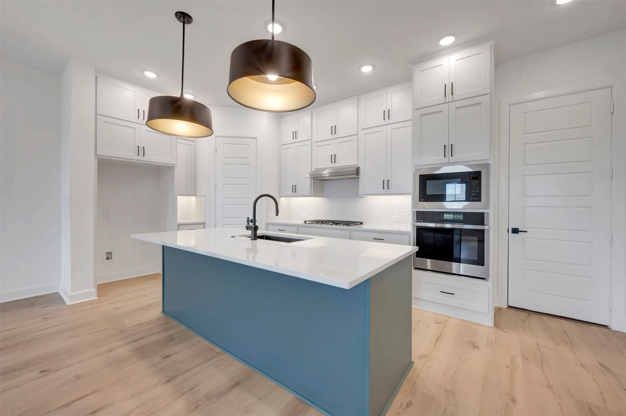 Contemporary kitchen featuring a prominent island with a white countertop and dark blue base, complemented by two large pendant lights