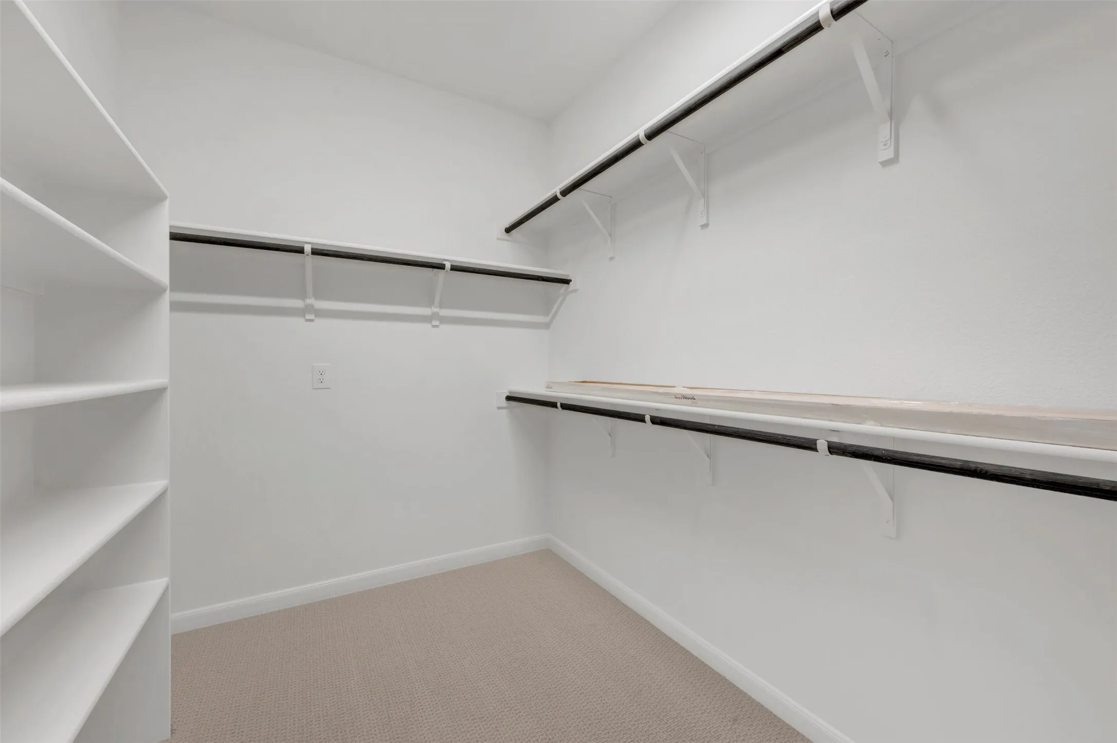 Walk-in closet featuring built-in shelving, multiple hanging rods, overhead storage shelves, and neutral carpeting