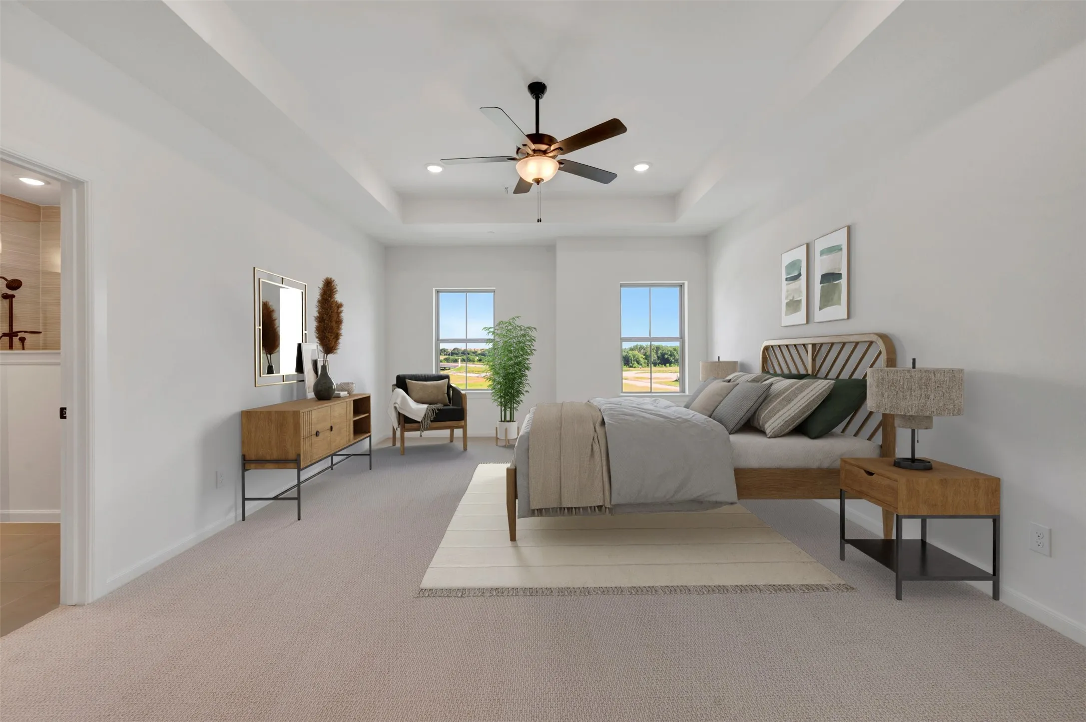 Spacious room featuring tray ceilings with a ceiling fan, two large windows, light-toned carpeting, and a doorway opening to a bathroom with a tiled shower