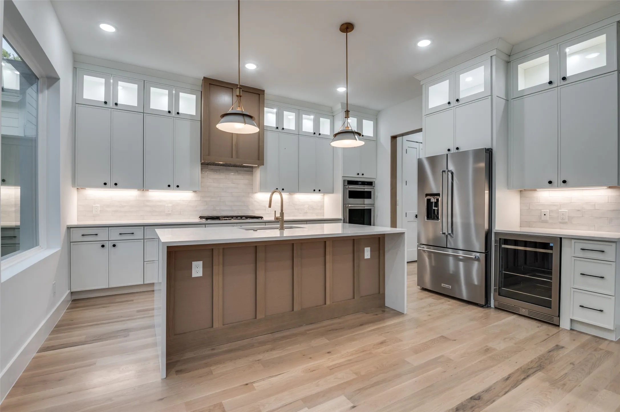 Kitchen featuring backsplash, stainless steel appliances, beverage cooler, light countertops, and light wood finished floors