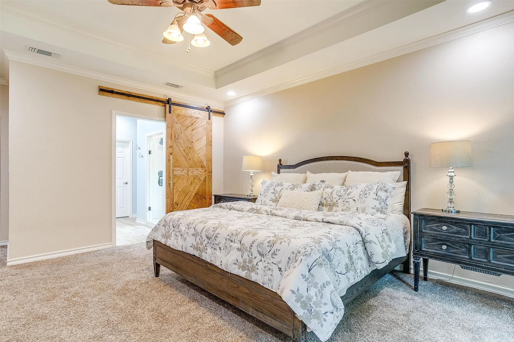 Bedroom featuring a barn door, crown molding, ceiling fan, light colored carpet, and a raised ceiling