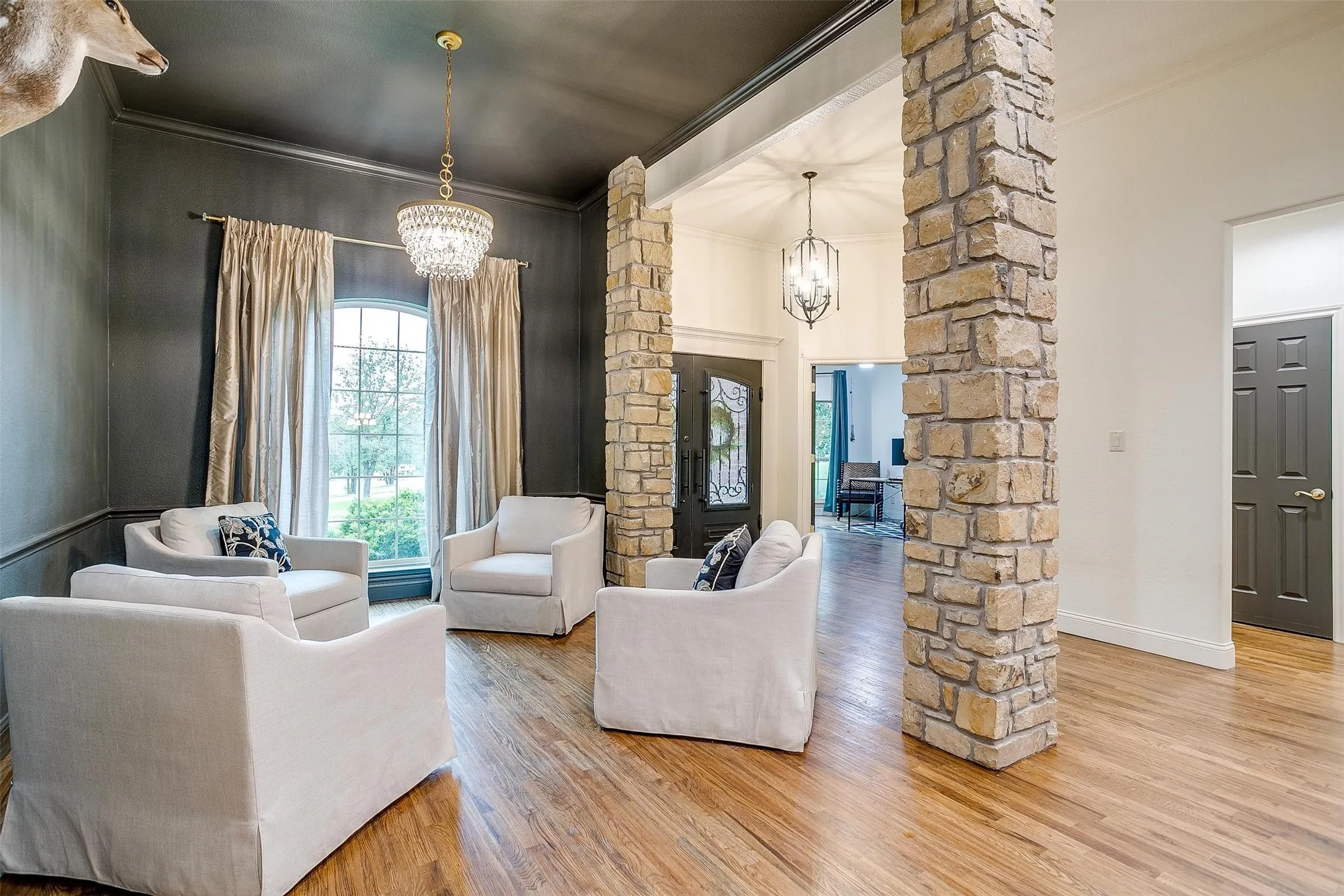 Living room with decorative columns, ornamental molding, suspended lighting, wood finished floors, and a high ceiling