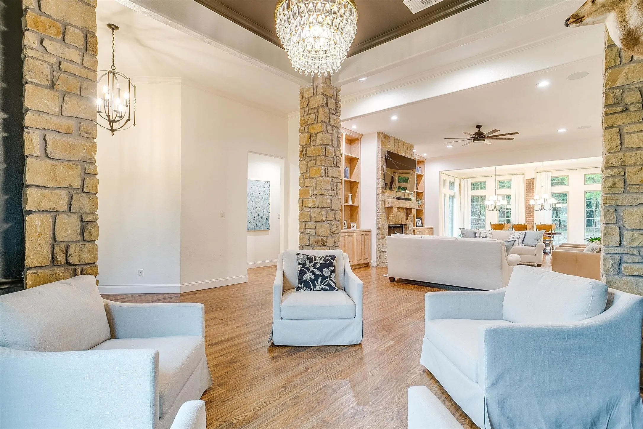 Living room featuring hanging lights, light wood-type flooring, built in features, ceiling fan, and a stone fireplace