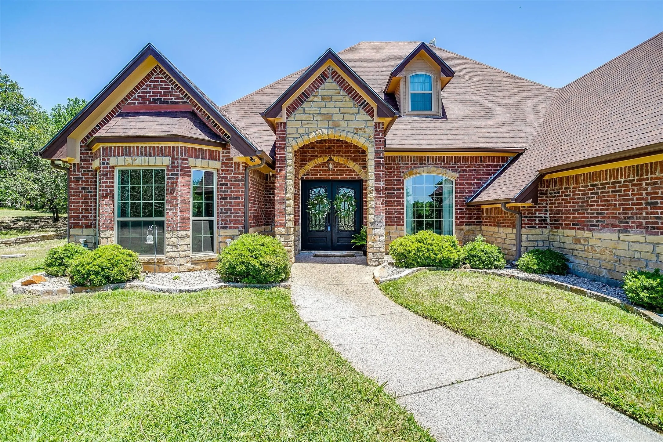 View of front of house with stone siding, roof with shingles, brick siding, and a front yard