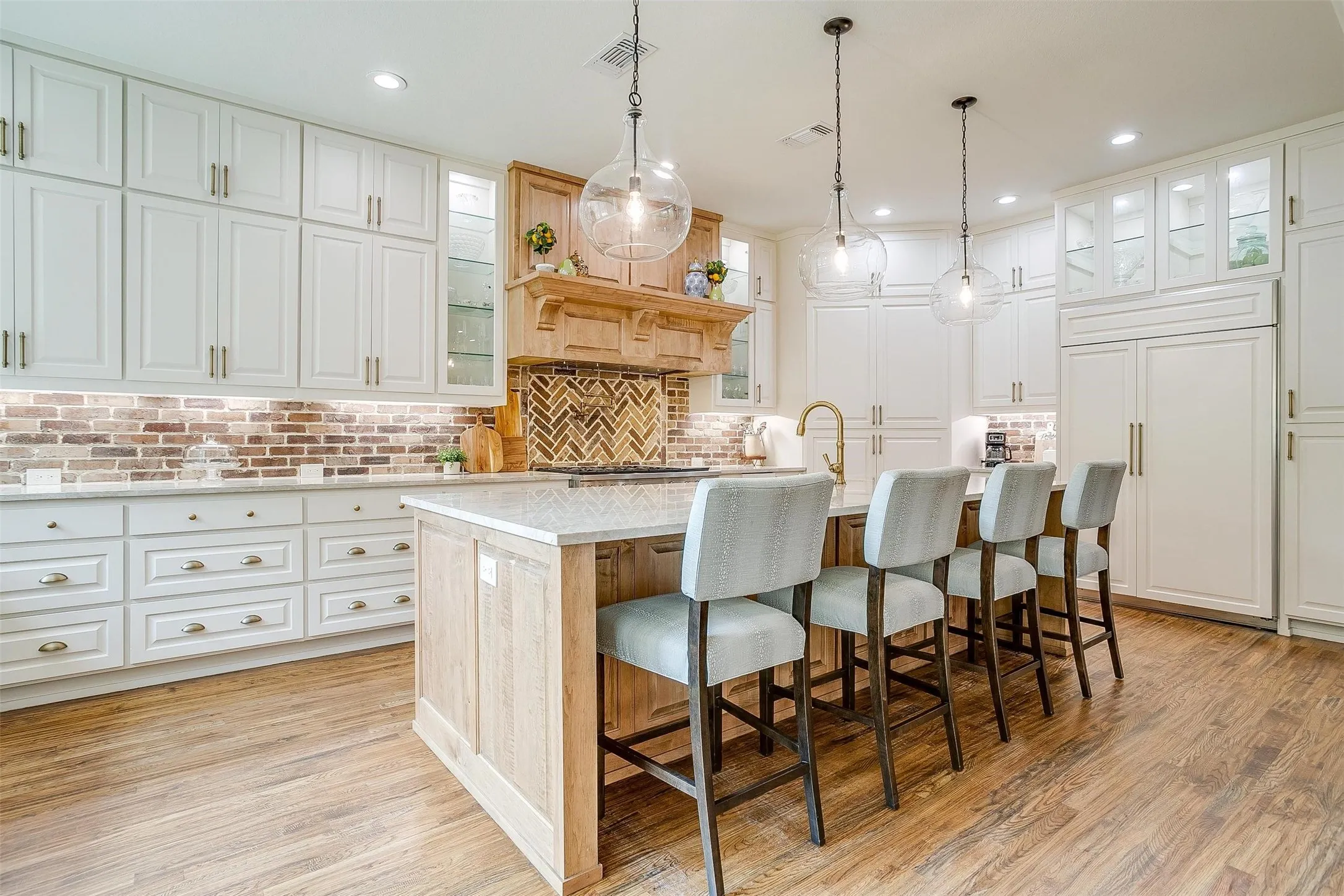 Dual tone kitchen with glass insert cabinets, pendant lighting, a breakfast bar area, a kitchen island with sink, and light wood-type flooring
