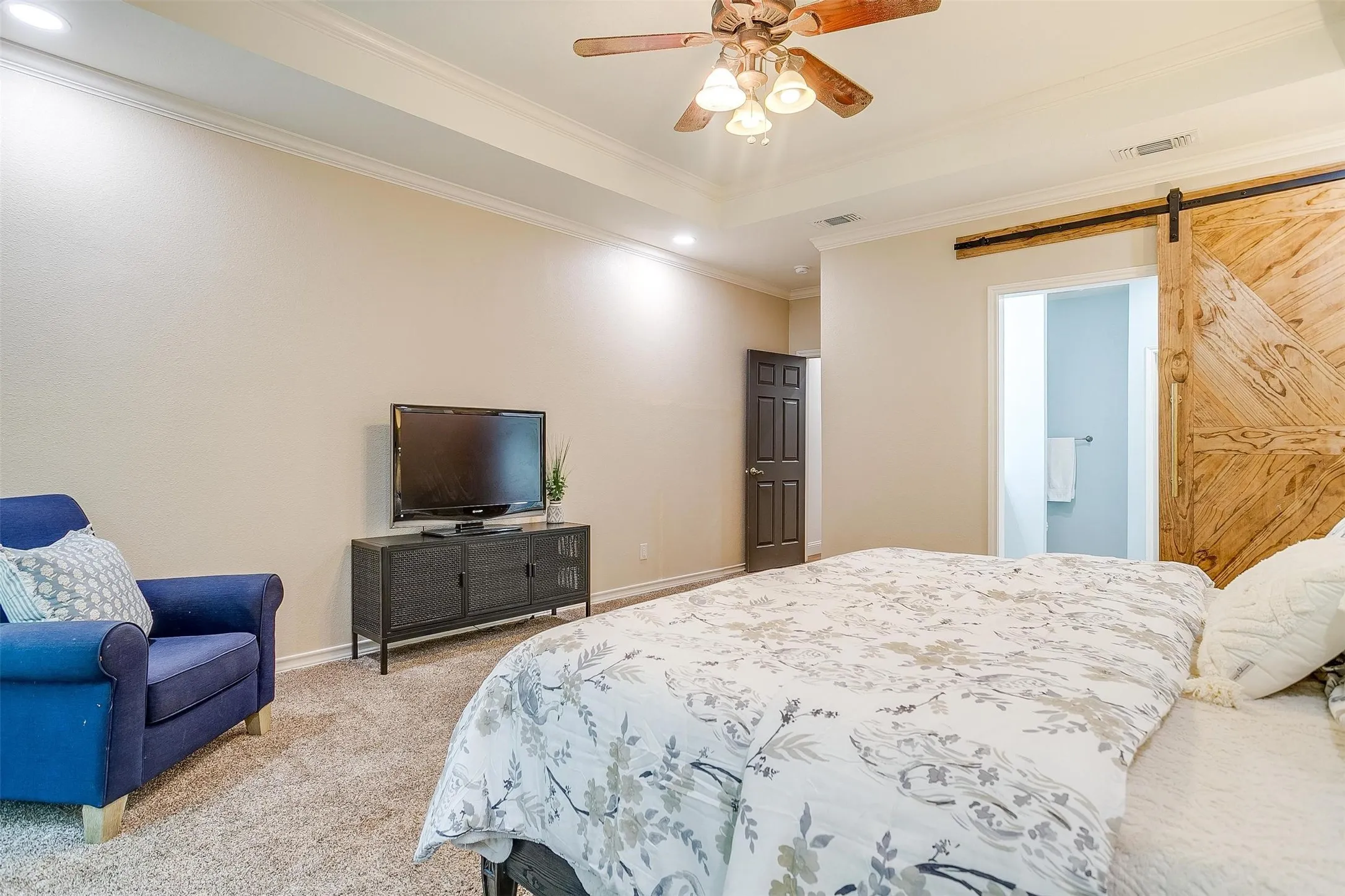 Carpeted bedroom featuring a barn door, a tray ceiling, ornamental molding, a ceiling fan, and recessed lighting